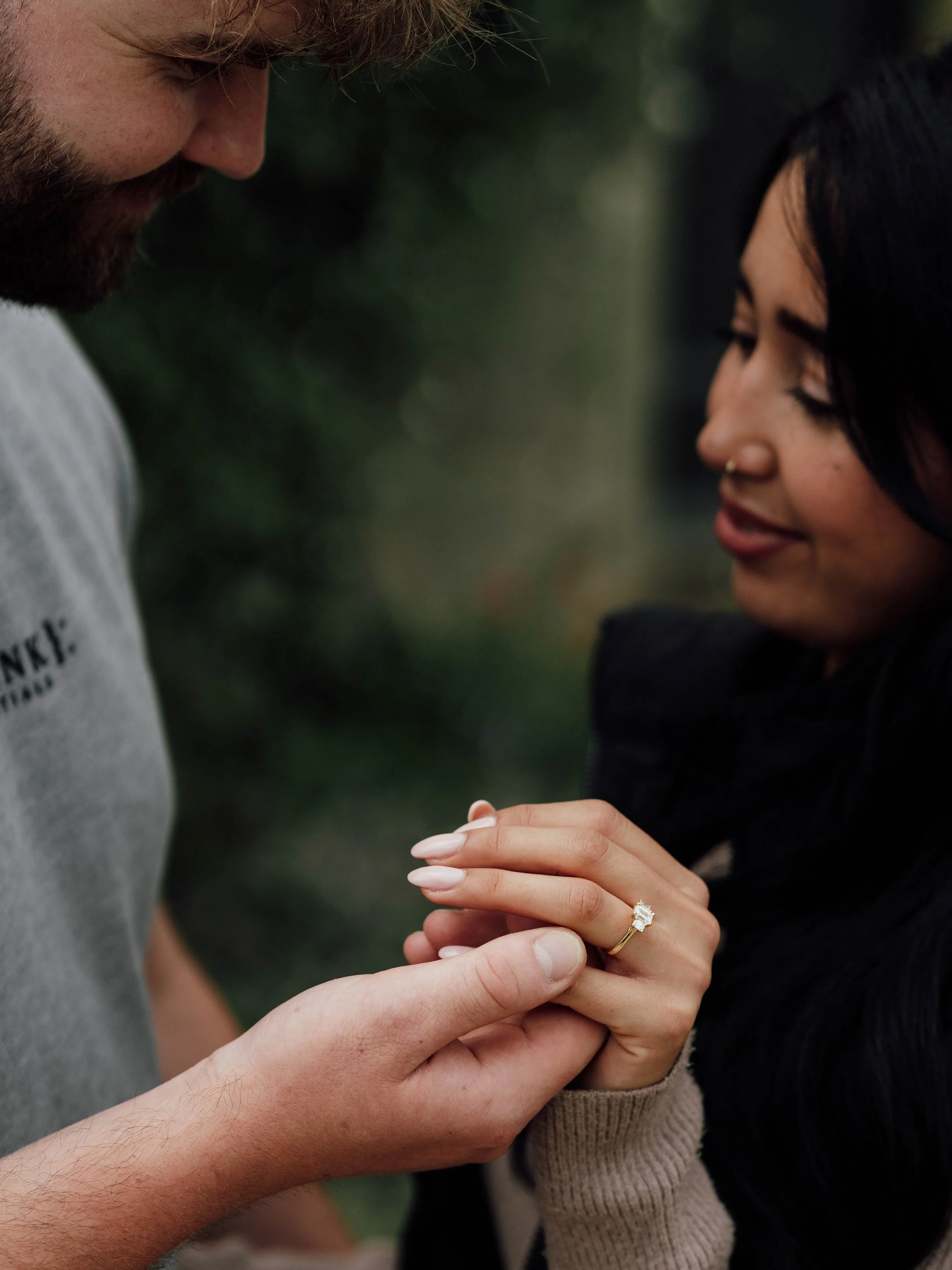 A man and a woman exchanging rings outdoors, with the man placing a ring on the woman's finger.