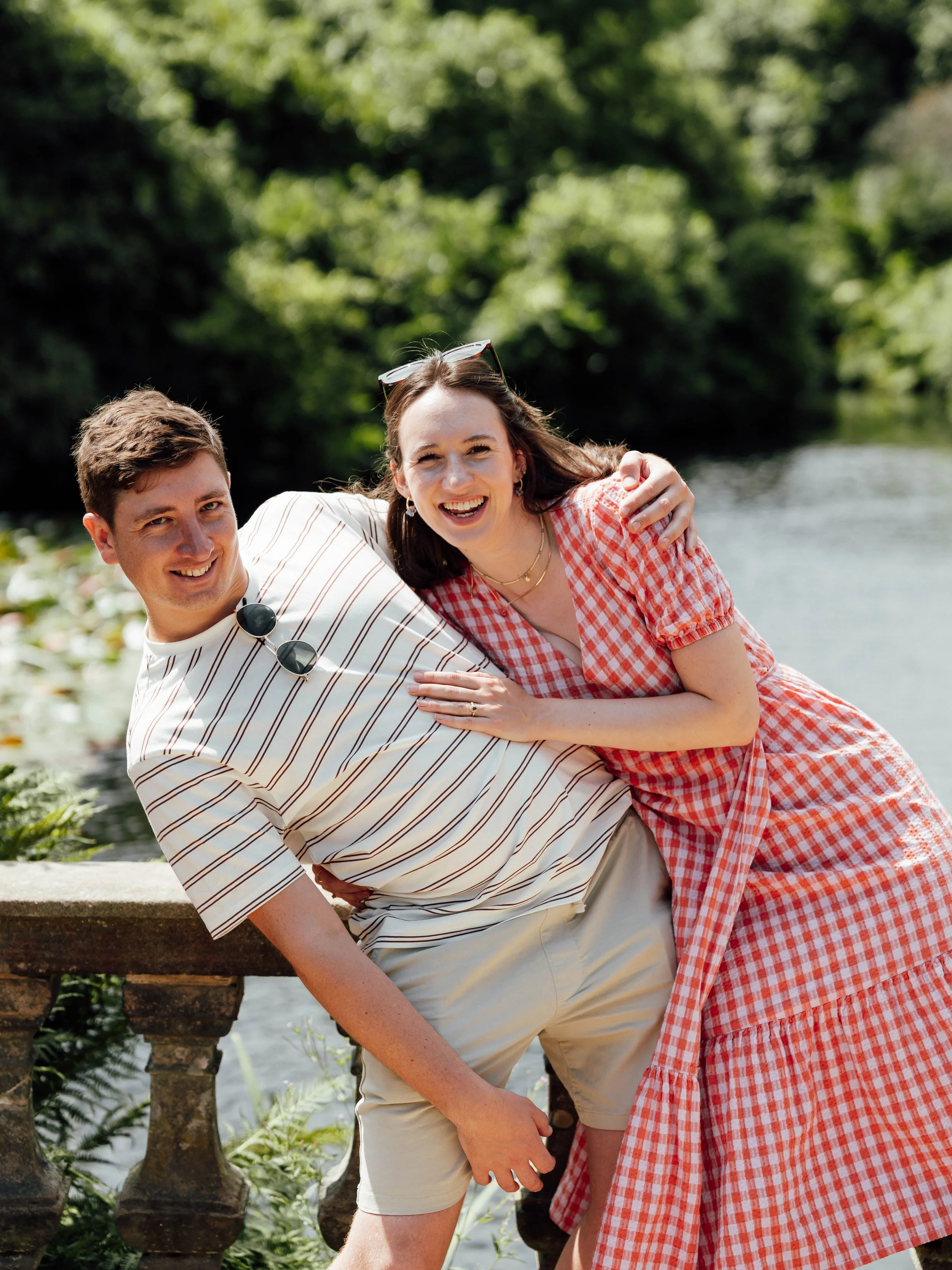 A man and woman smiling and enjoying their time outdoors near a water body with trees in the background.