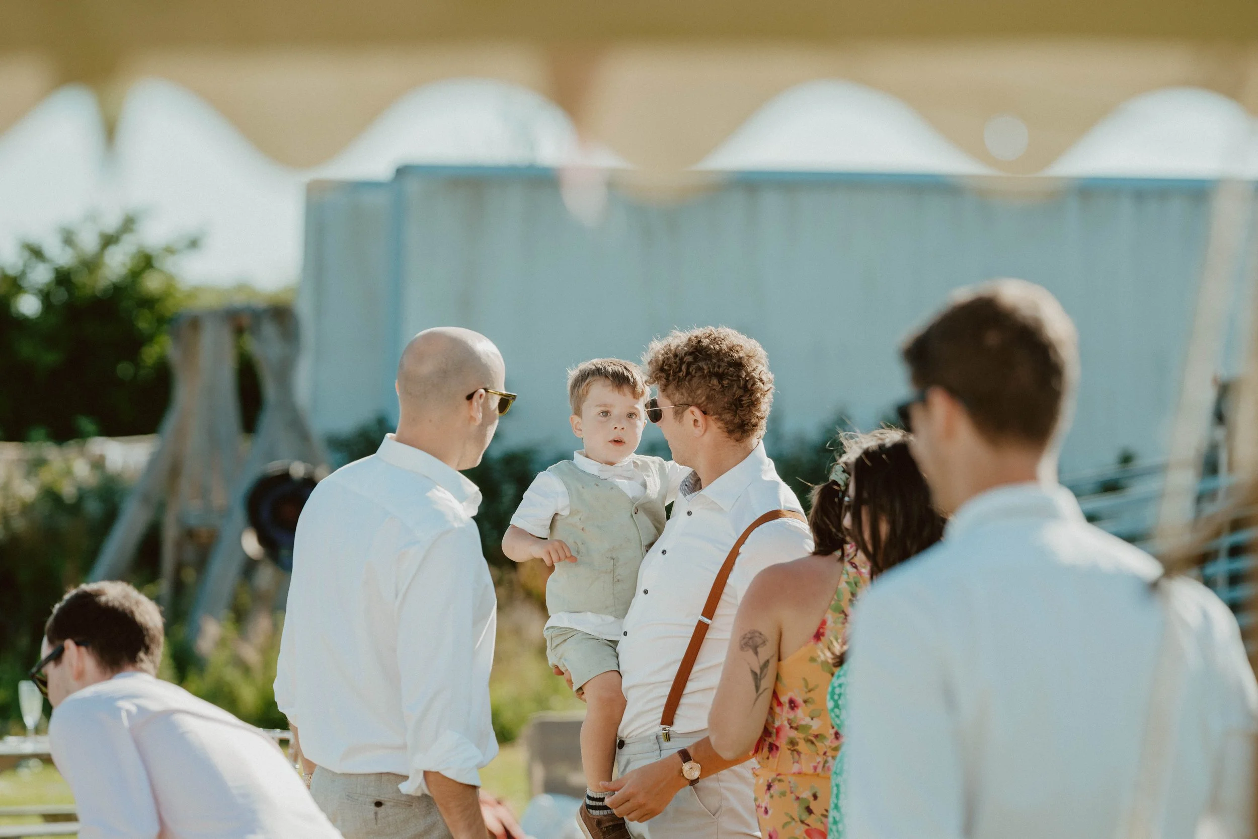 Young man holding a child, surrounded by adults, outdoors on a sunny day