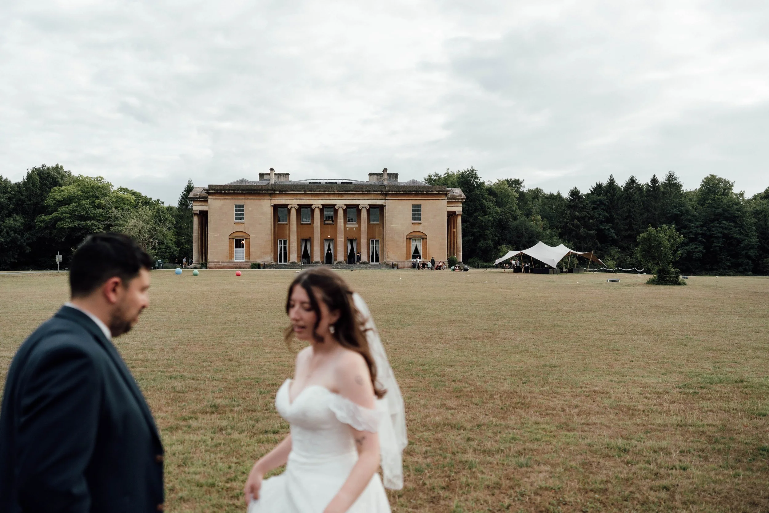 A bride and groom standing on a lawn in front of a large historic building during an outdoor wedding.