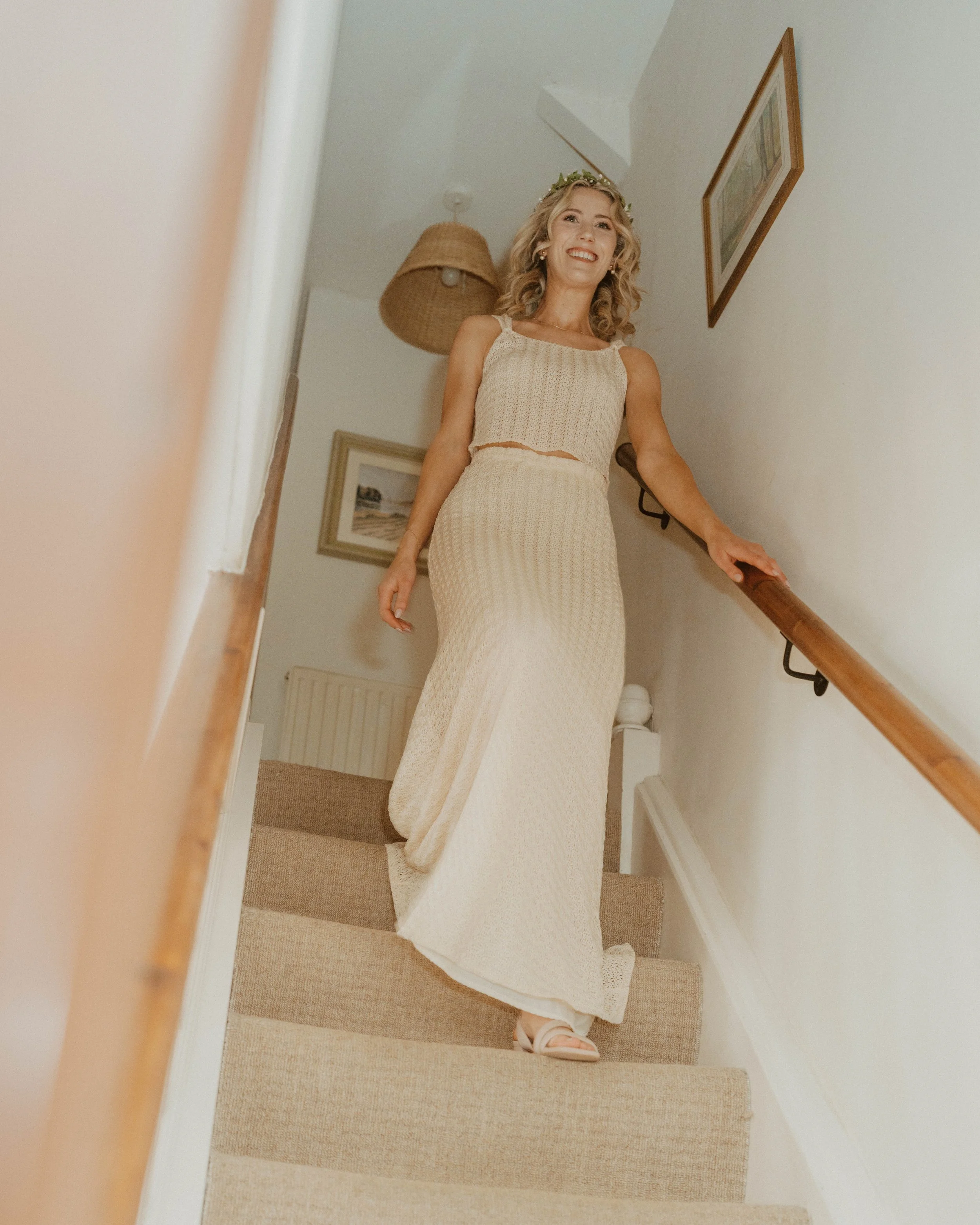 Woman in a cream-colored knit dress with a floral headband walking down carpeted stairs, smiling.