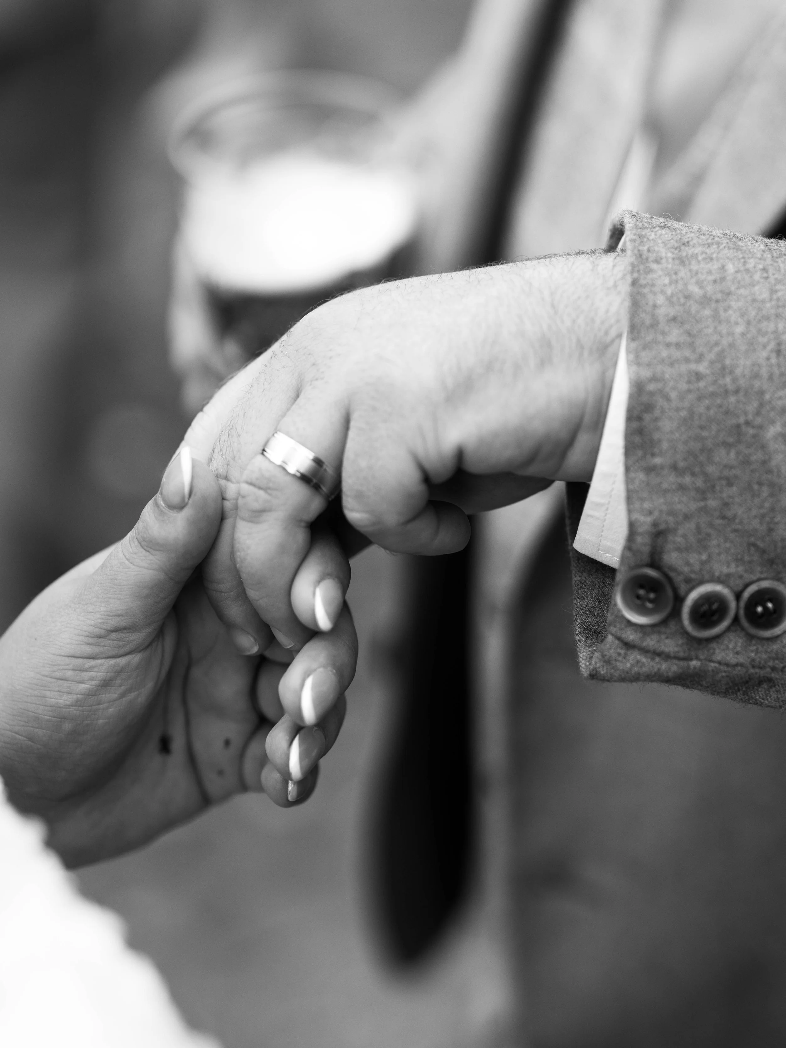 Close-up of two people holding hands in a handshake, with one person wearing a suit jacket with buttons and the other wearing a ring.