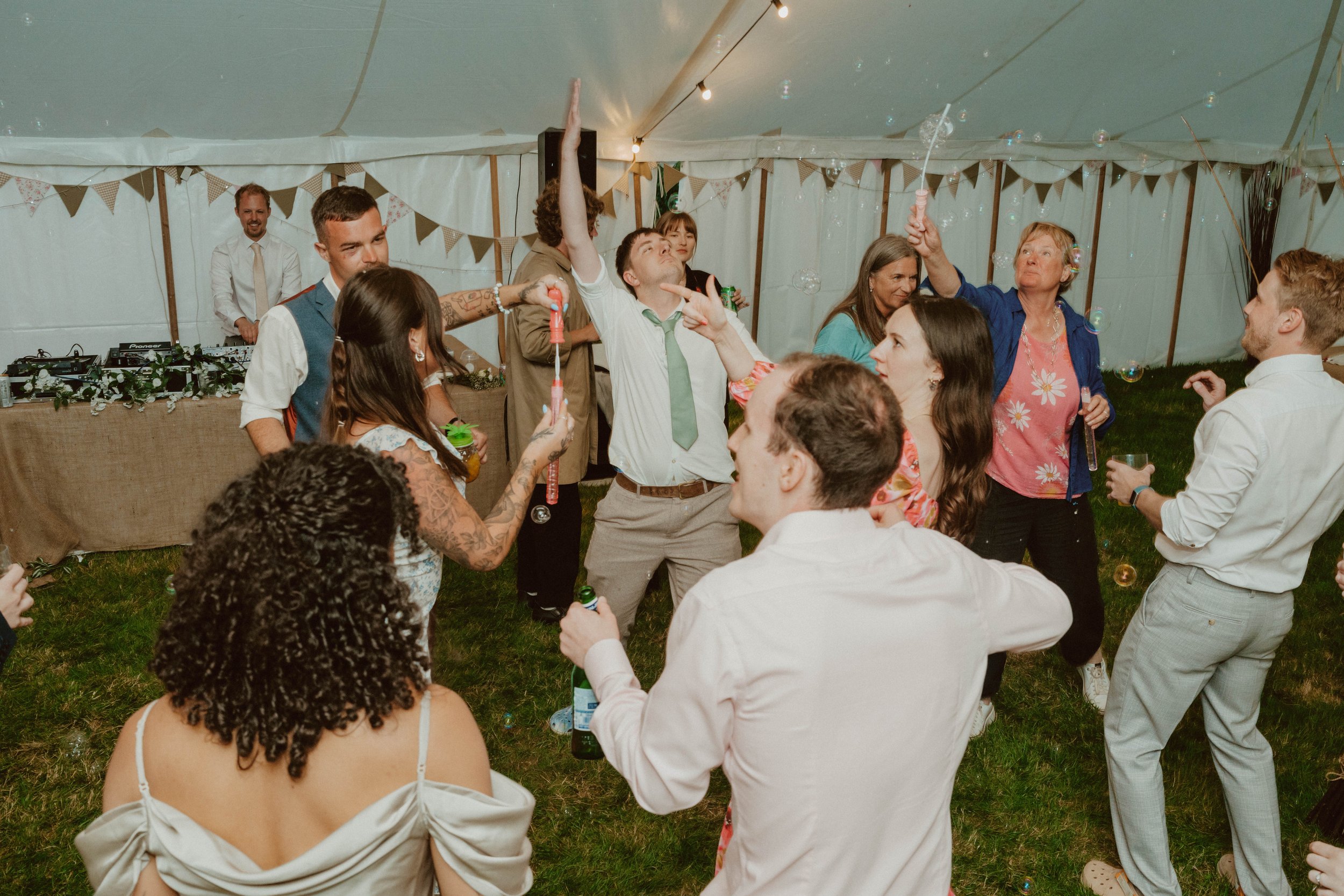 People enjoying a lively dance and celebration inside a large tent decorated with bunting at a party or wedding.