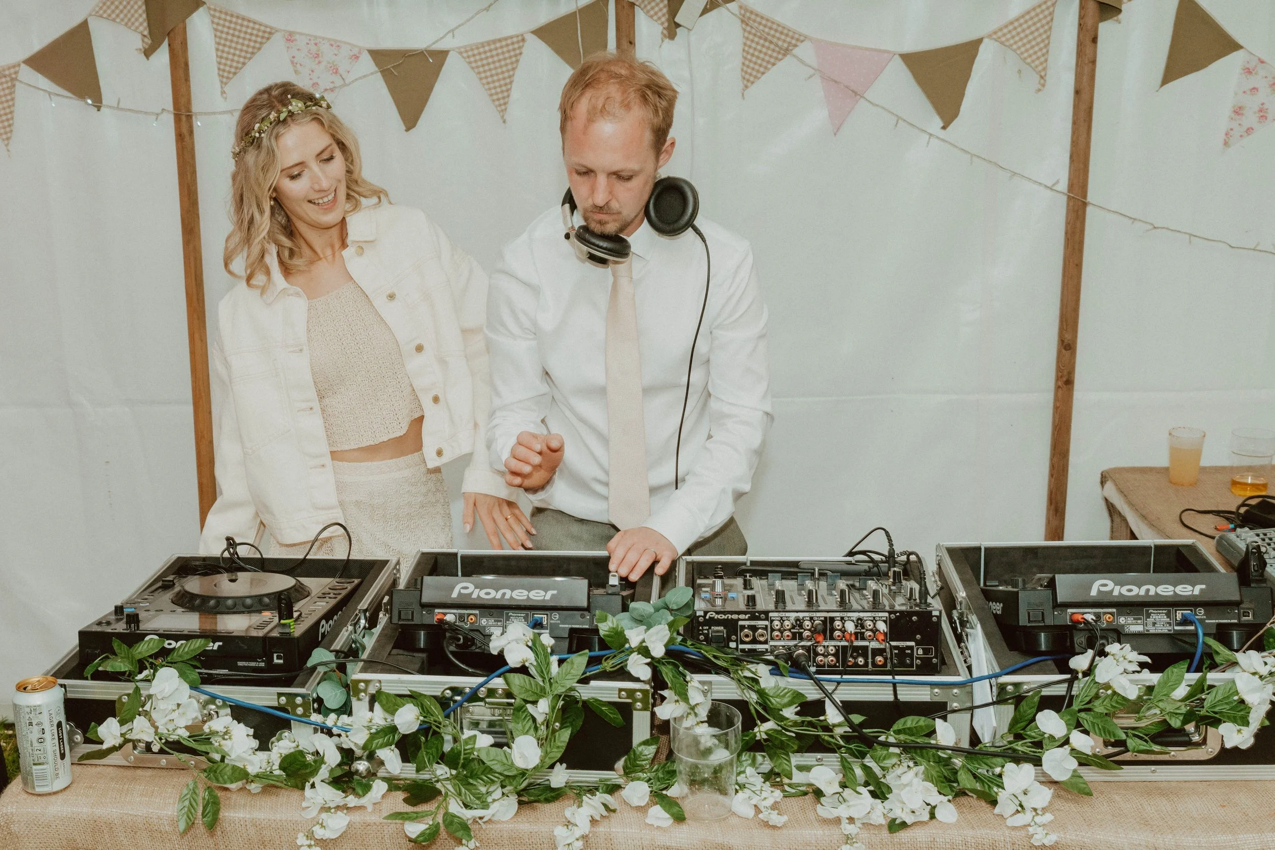 A man DJing with a woman dancing at a decorated party or wedding reception.