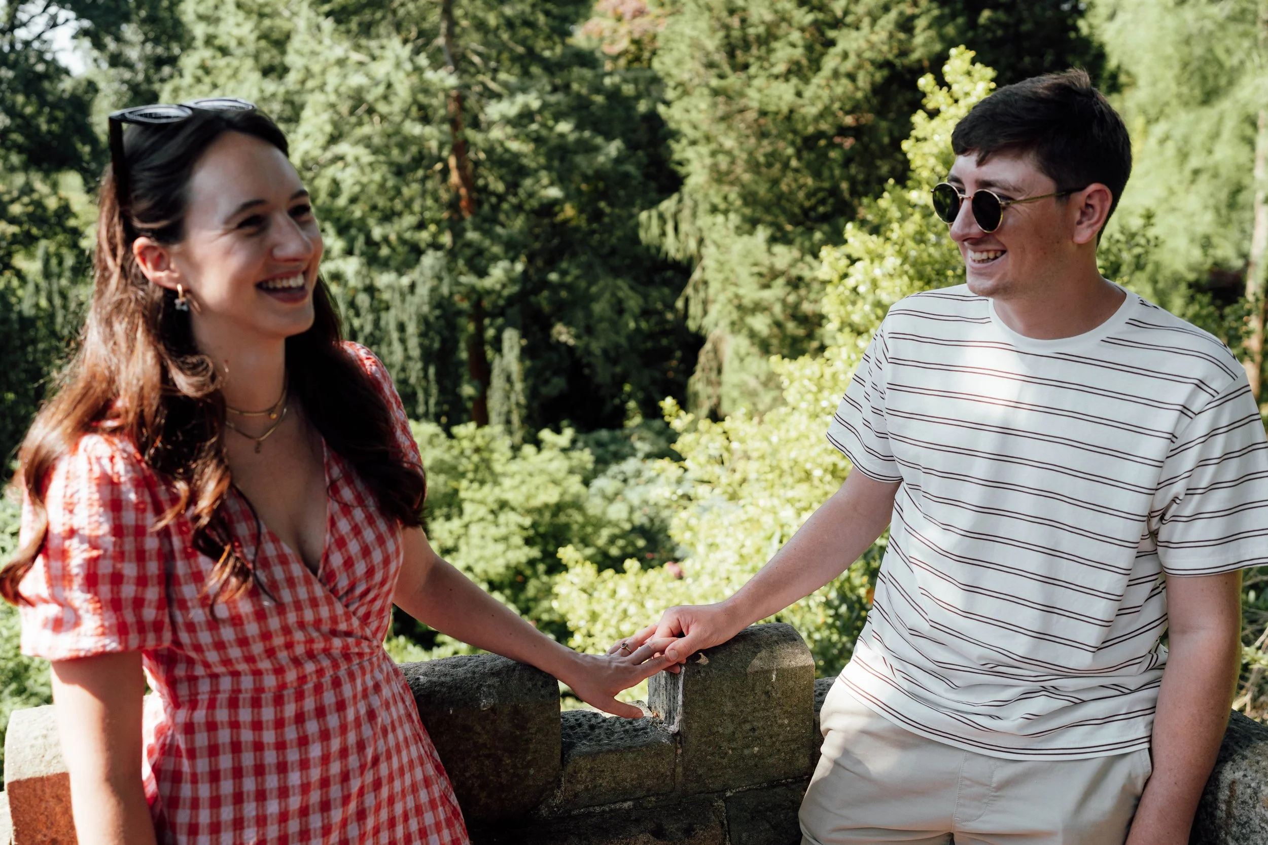 A smiling woman and man holding hands outdoors in a lush green park.