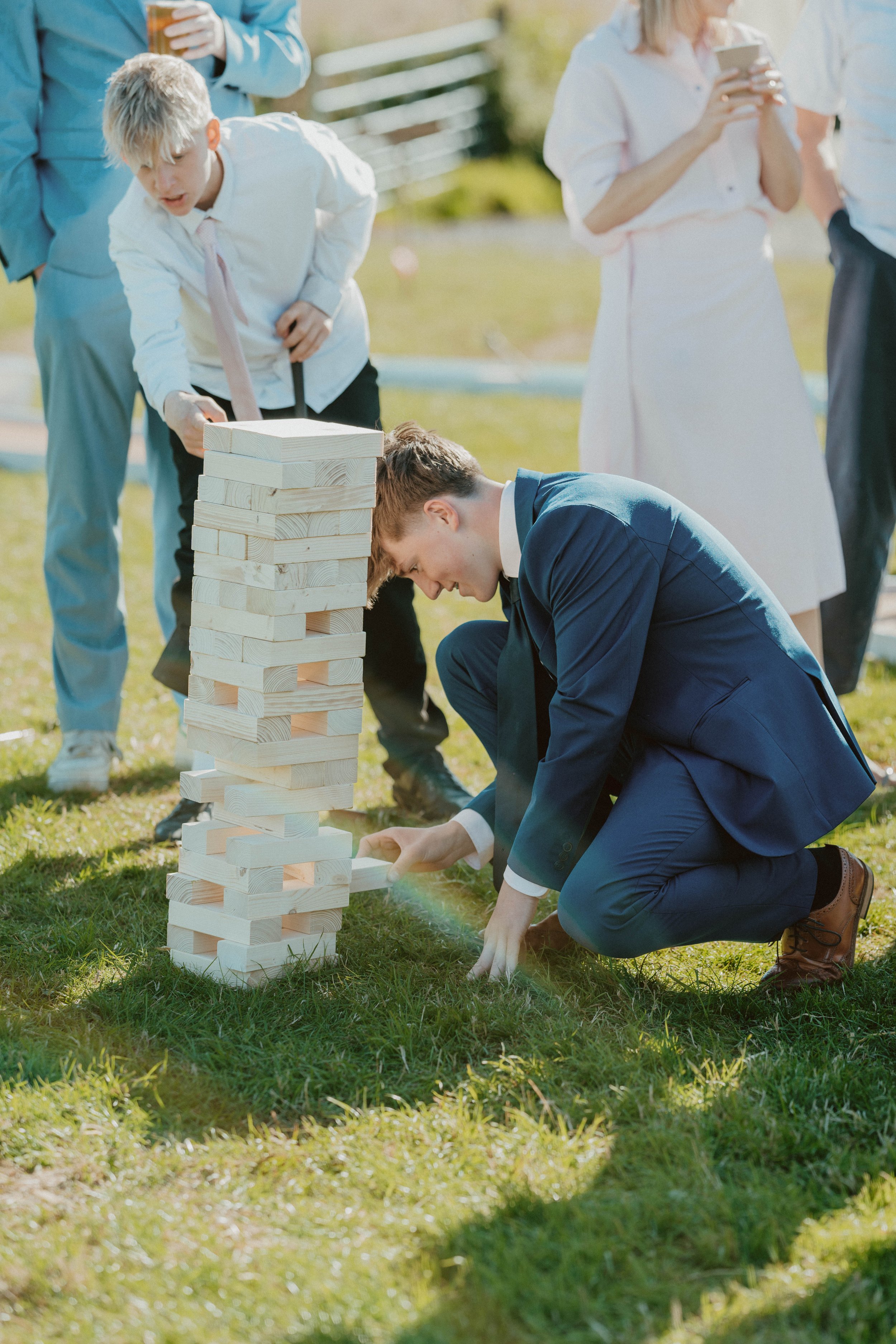 A group of people playing a giant outdoor Jenga game on grass during daytime.