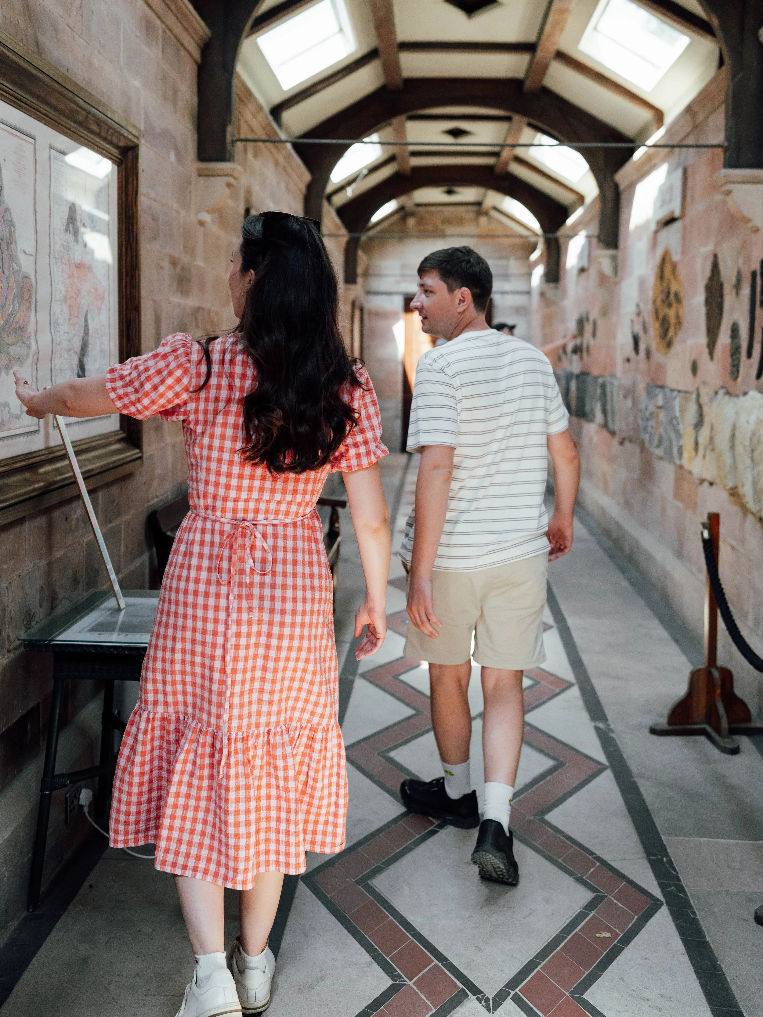 Two people walking through an art gallery or museum with a woman pointing at artwork on the wall.