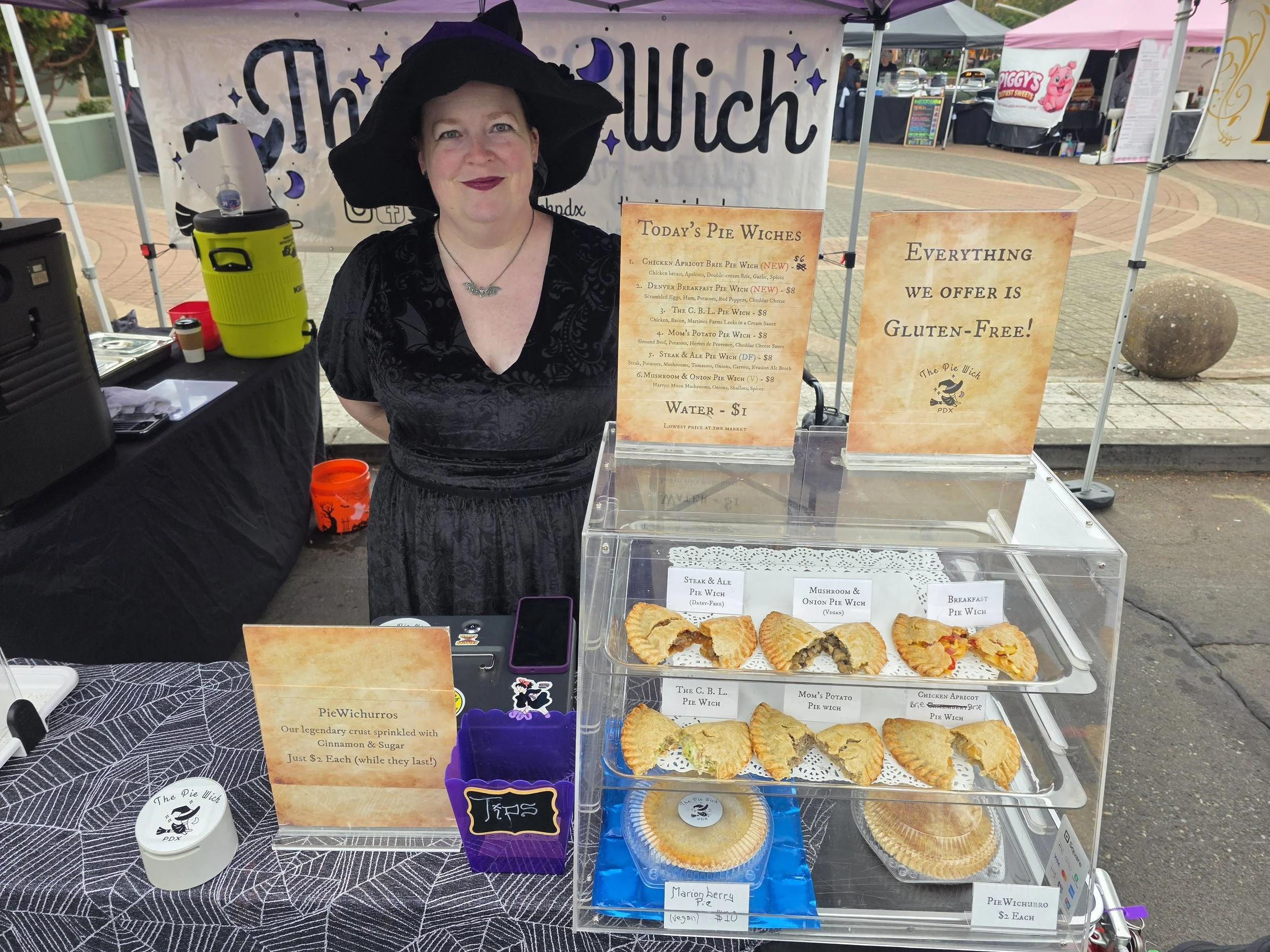Mrs. Wich at the Pie Wich booth at the Gresham Farmers' Market, with several pies in a display case.