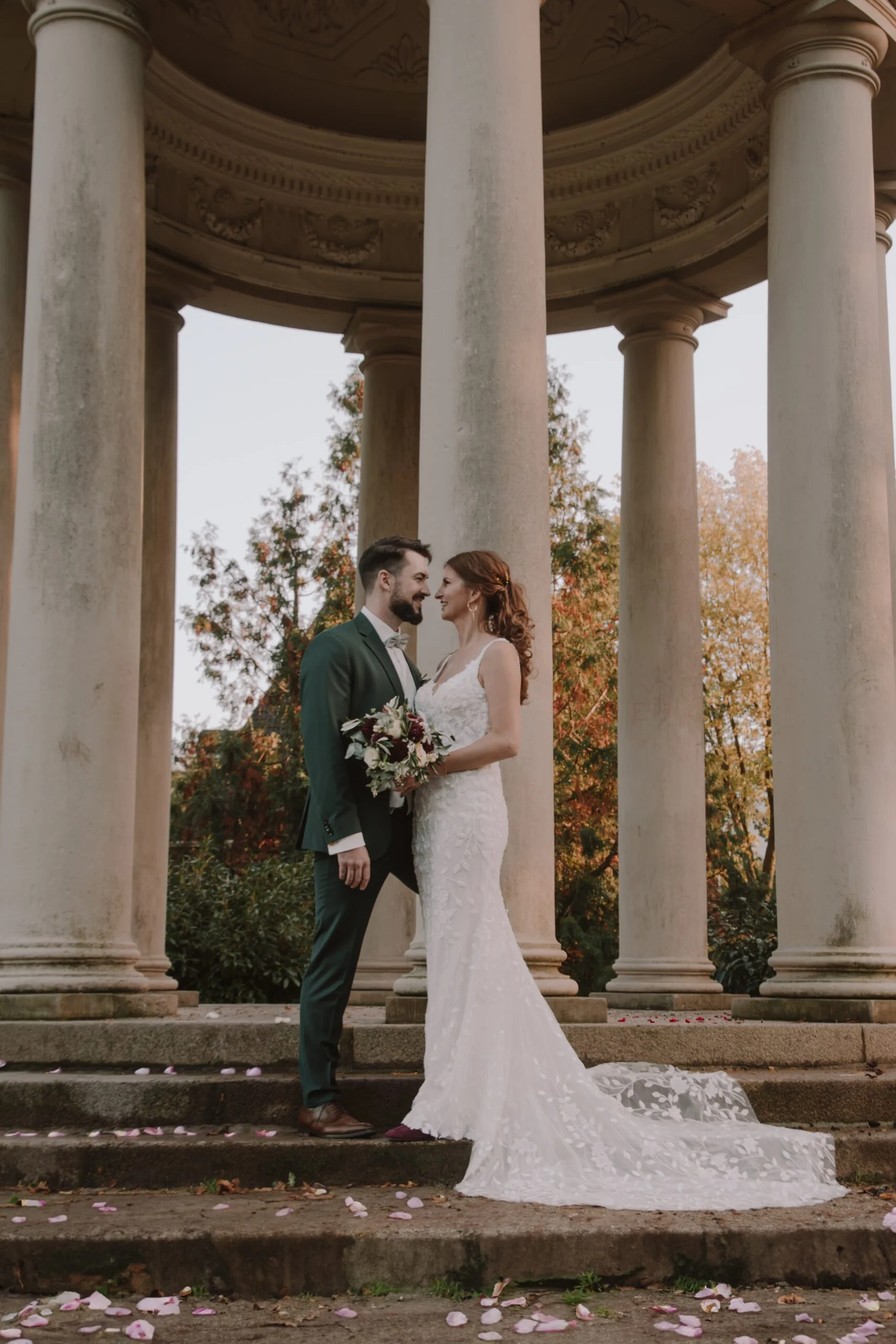 Eutin. Braut und Bräutigam stehen vor einer historischen Säulenhalle, umgeben von Herbstbäumen, beim Hochzeitsshooting / Brautpaarshooting.
