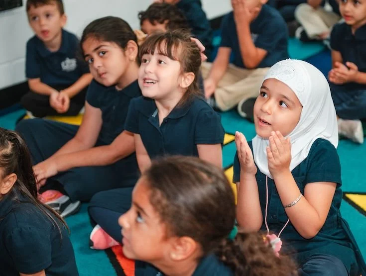 Group of diverse school children in uniform sitting on the floor and listening attentively in a classroom.