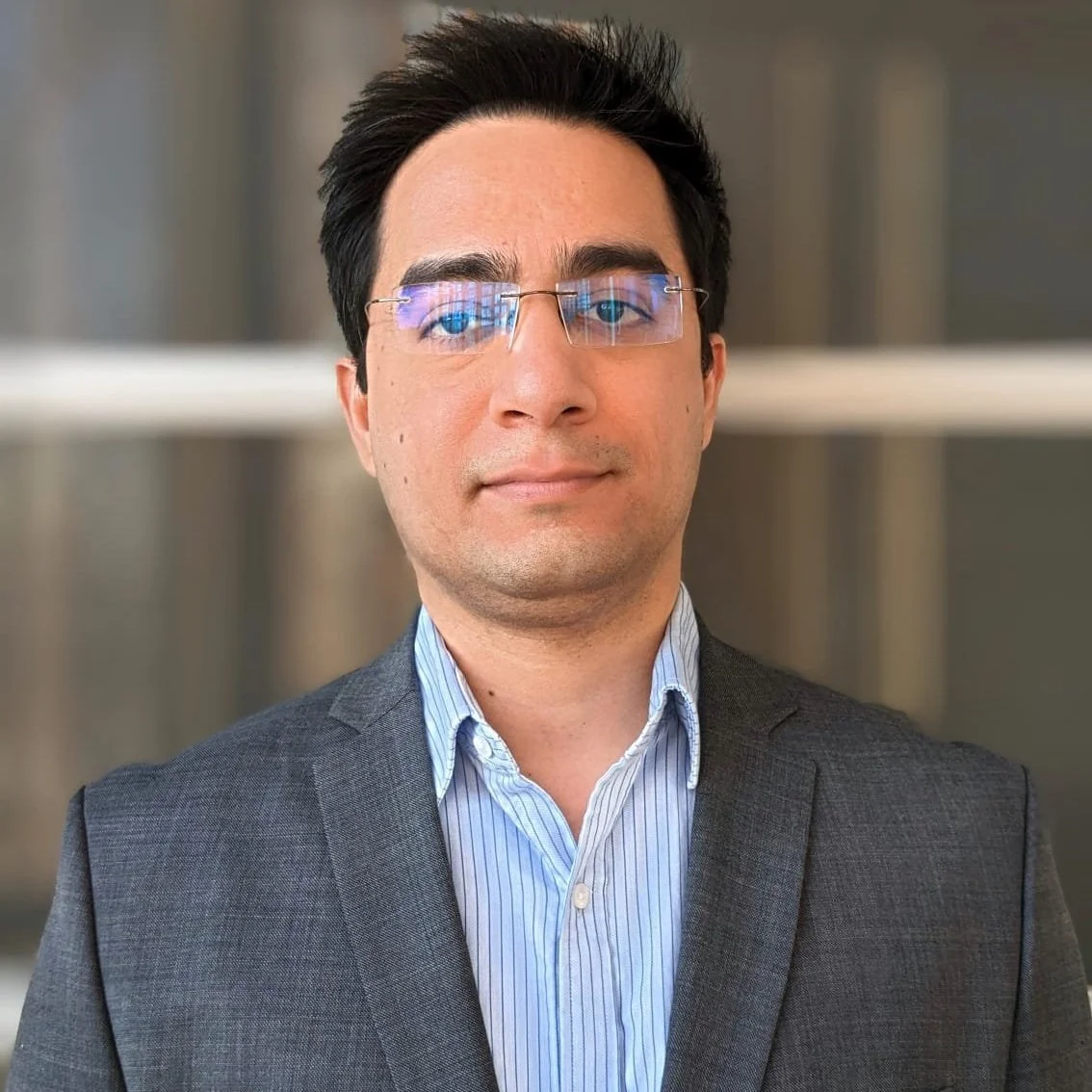 Akshay Kaushik formal portrait in a grey suit jacket and light blue, open collared shirt