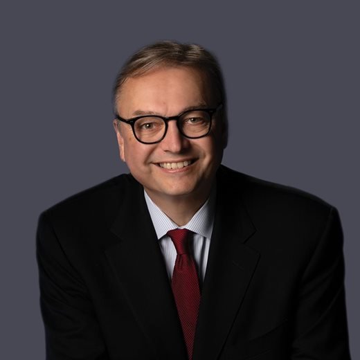 Mervon Mehta portrait in a dark suit, white shirt, and red tie