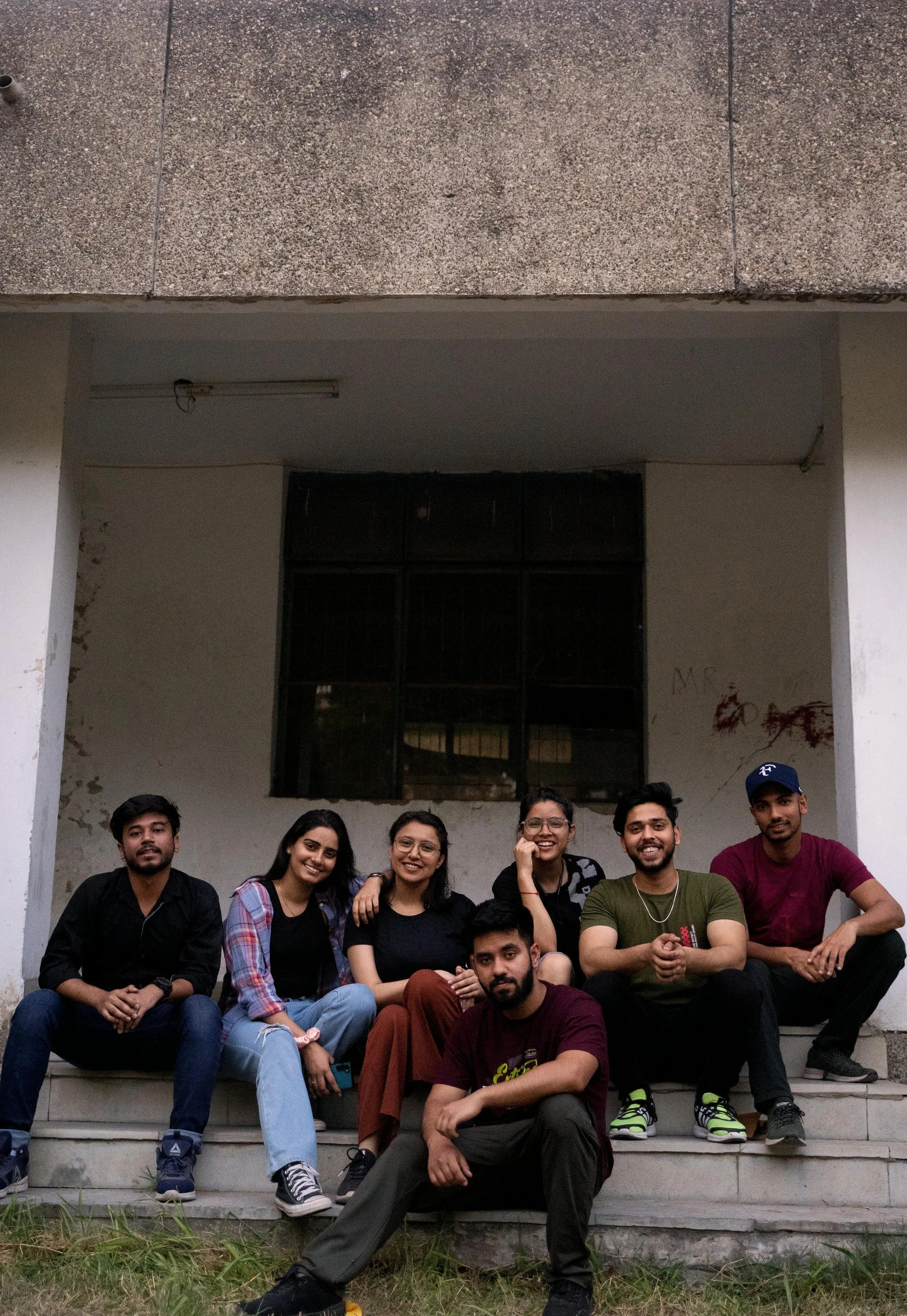 Group of six South Asian people sitting on steps outside a building.