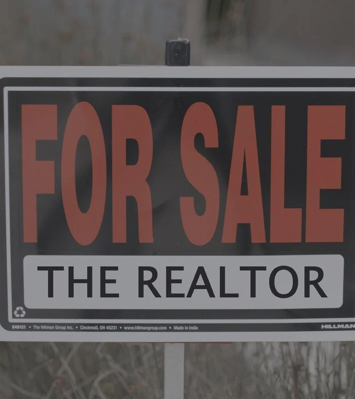 A for sale sign with black, white, and orange colors that reads "FOR SALE THE REALTOR."