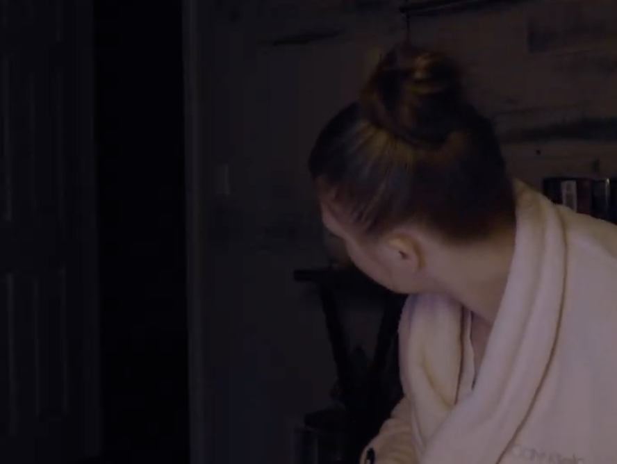 A woman staring into the darkness of an open door.