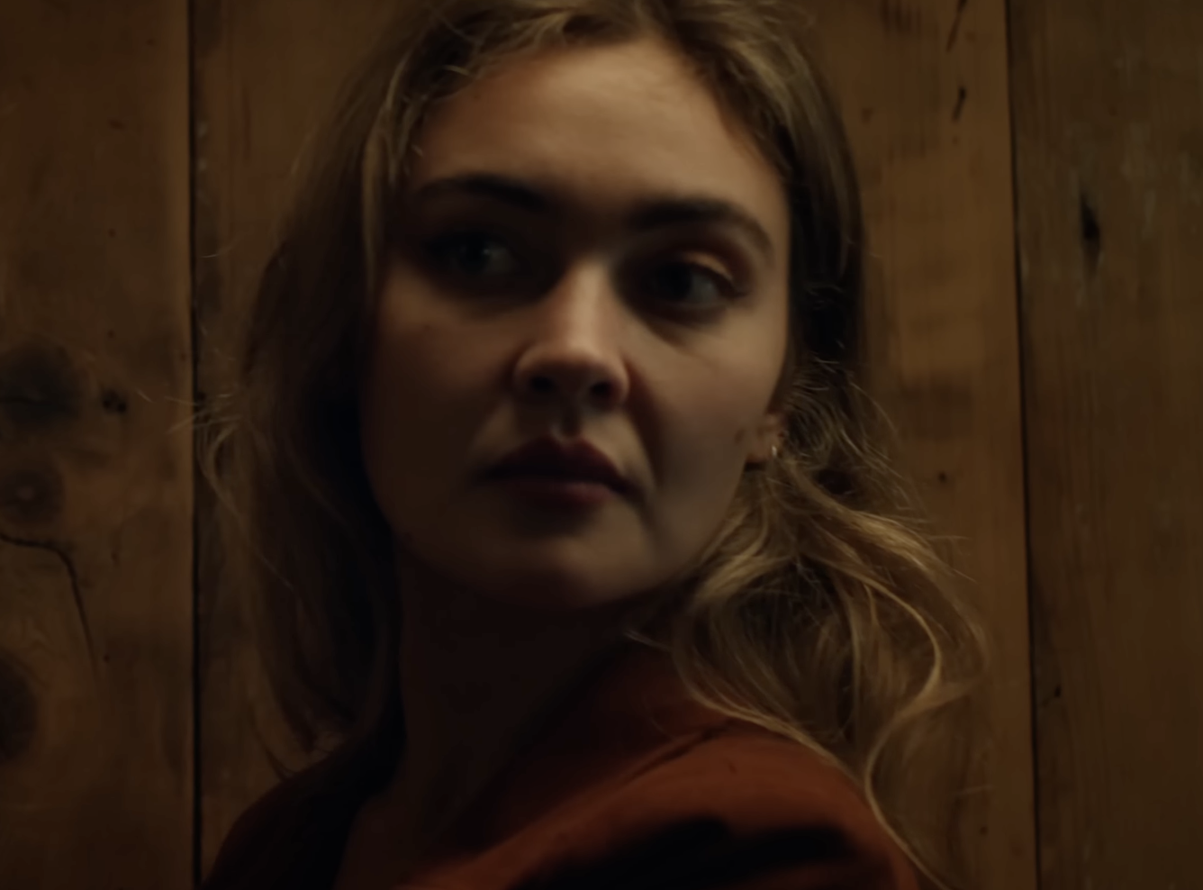 A dark-colored pair of pants and a white shirt with black accents lying on a forest ground covered with leaves, twigs, and green plants.