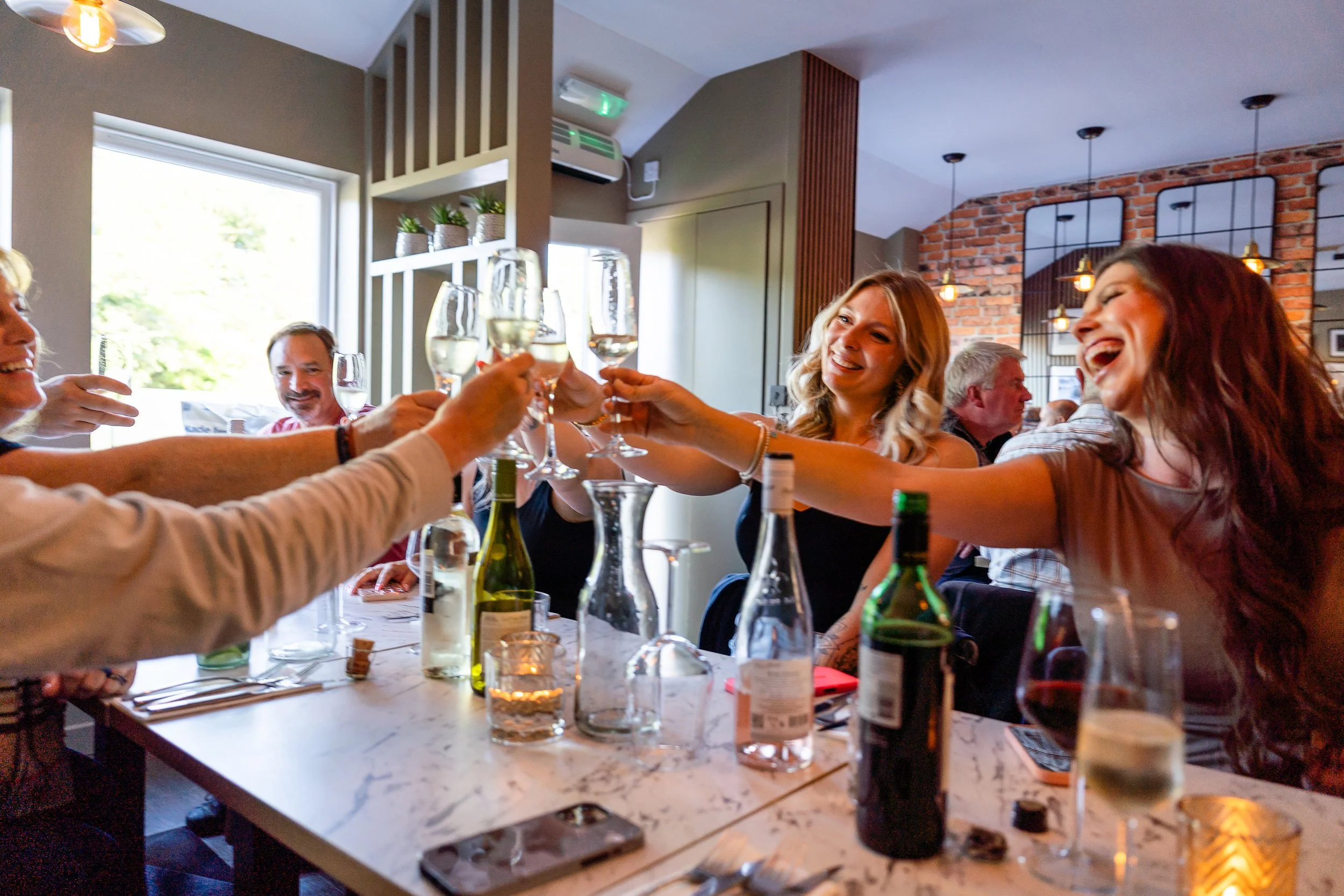 Group of people celebrating and clinking wine glasses at a restaurant table.