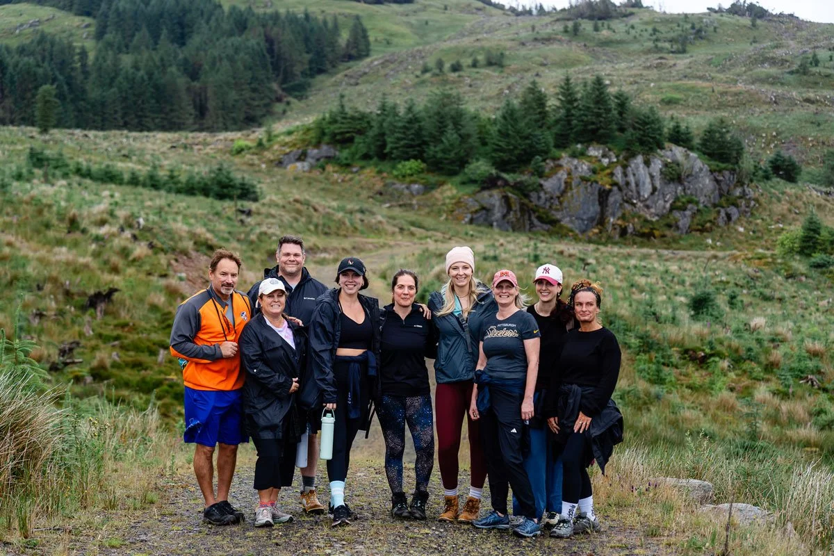 Group of nine people standing outdoors in a lush, green mountainous landscape, smiling at the camera.