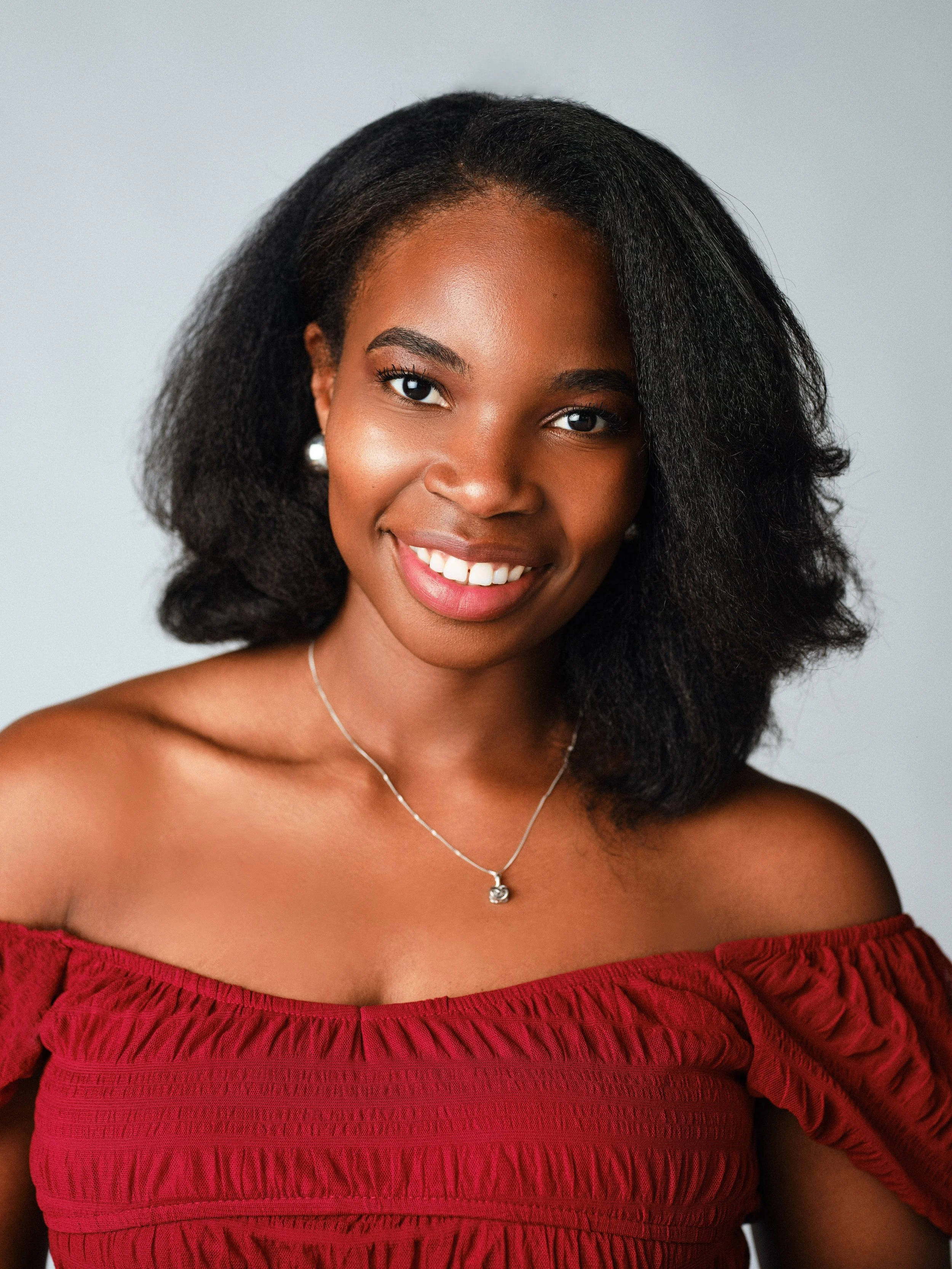 A woman with dark braided hair wearing a beige sweater sitting beside red berries and green foliage.