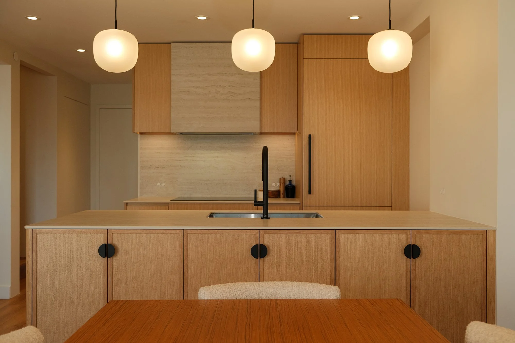 Modern kitchen with wooden cabinets, island, black sink faucet, three pendant lights, and beige walls.