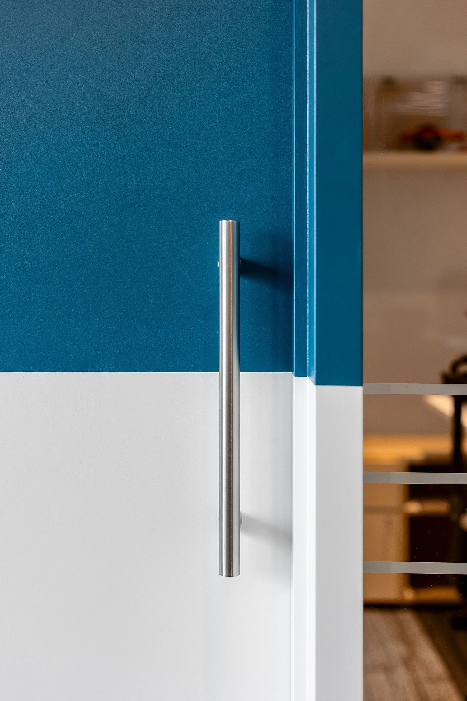Close-up of a modern blue door with a silver handle, partially open revealing a blurred interior space with shelves and objects.