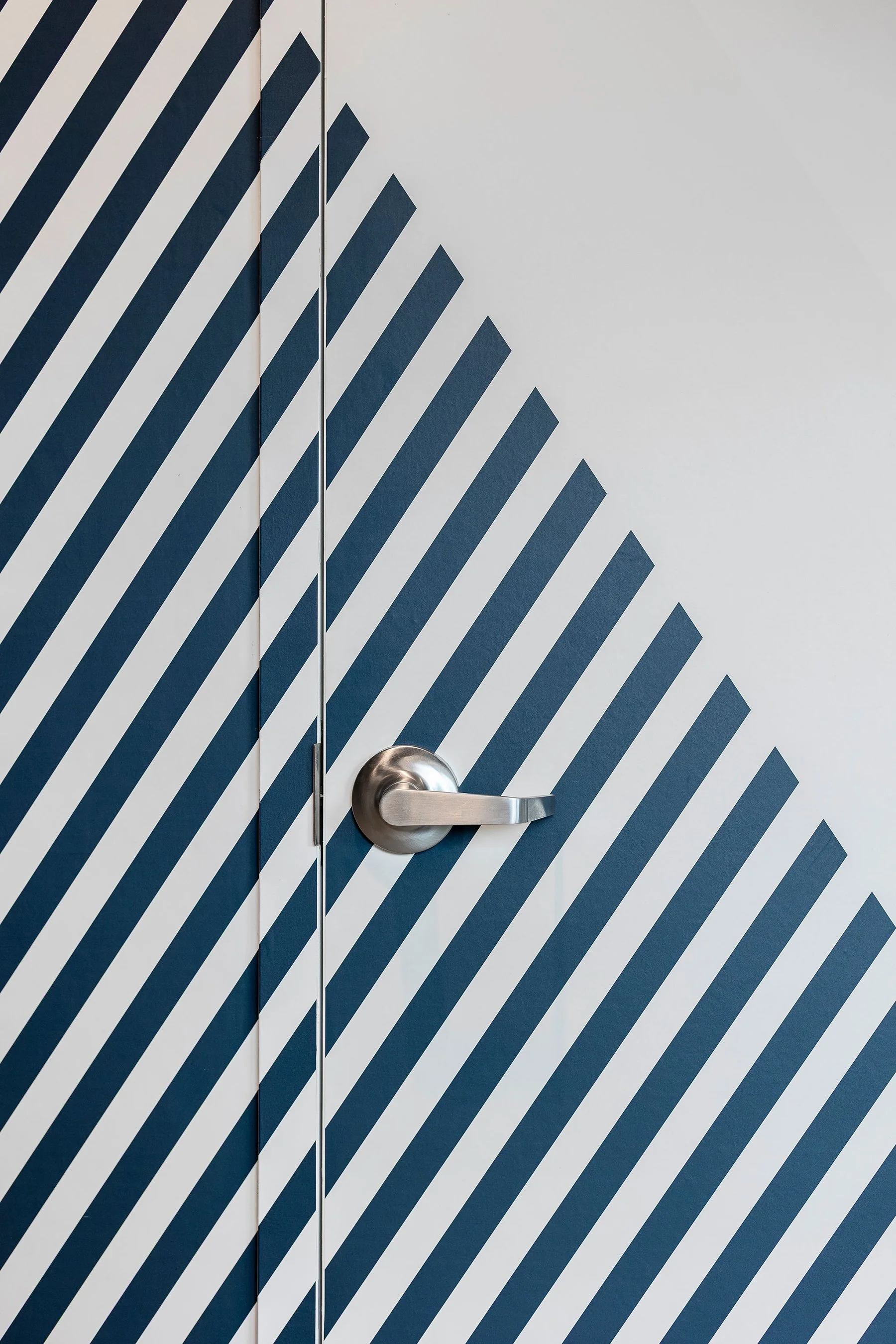 Door with a silver handle and a geometric pattern of dark blue and white diagonal lines on the surface.