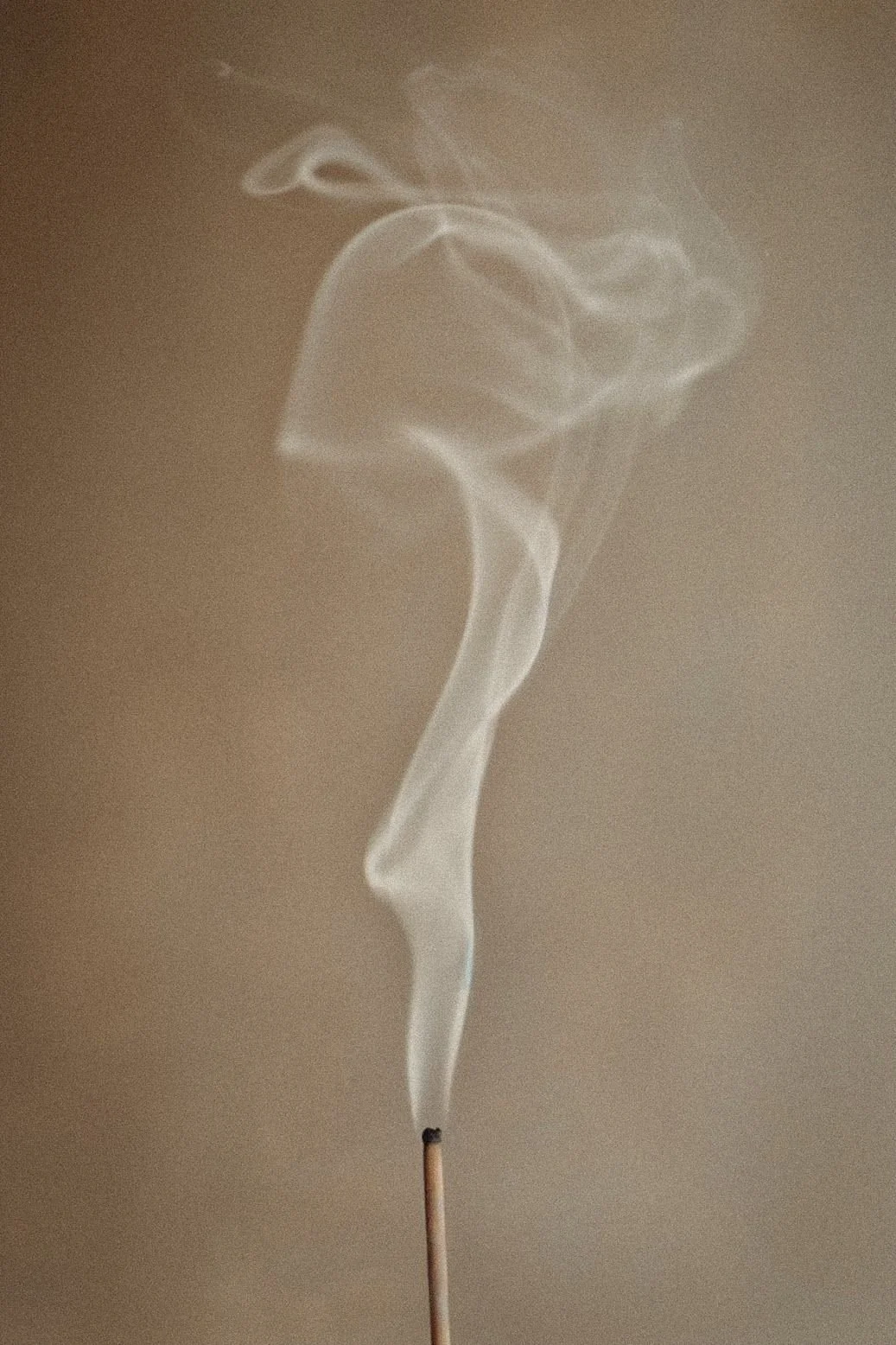 A lit incense stick with smoke curling upward in a spiral pattern.