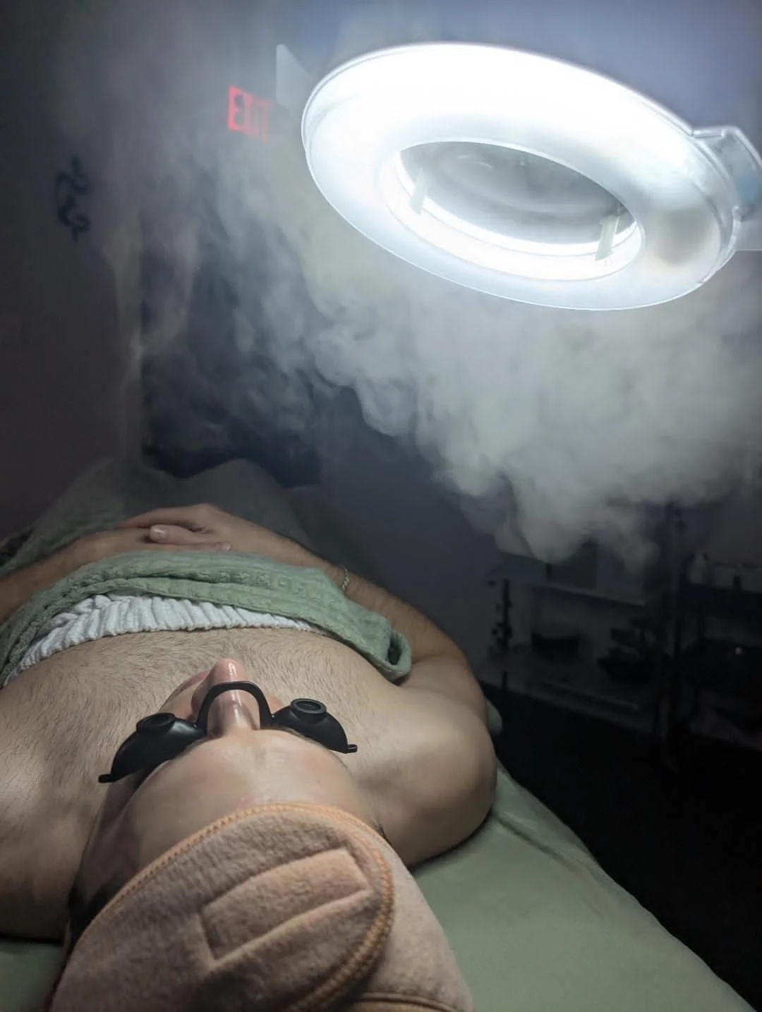 Person lying on an examination table under a circular MRI machine with a bright light in a medical facility.