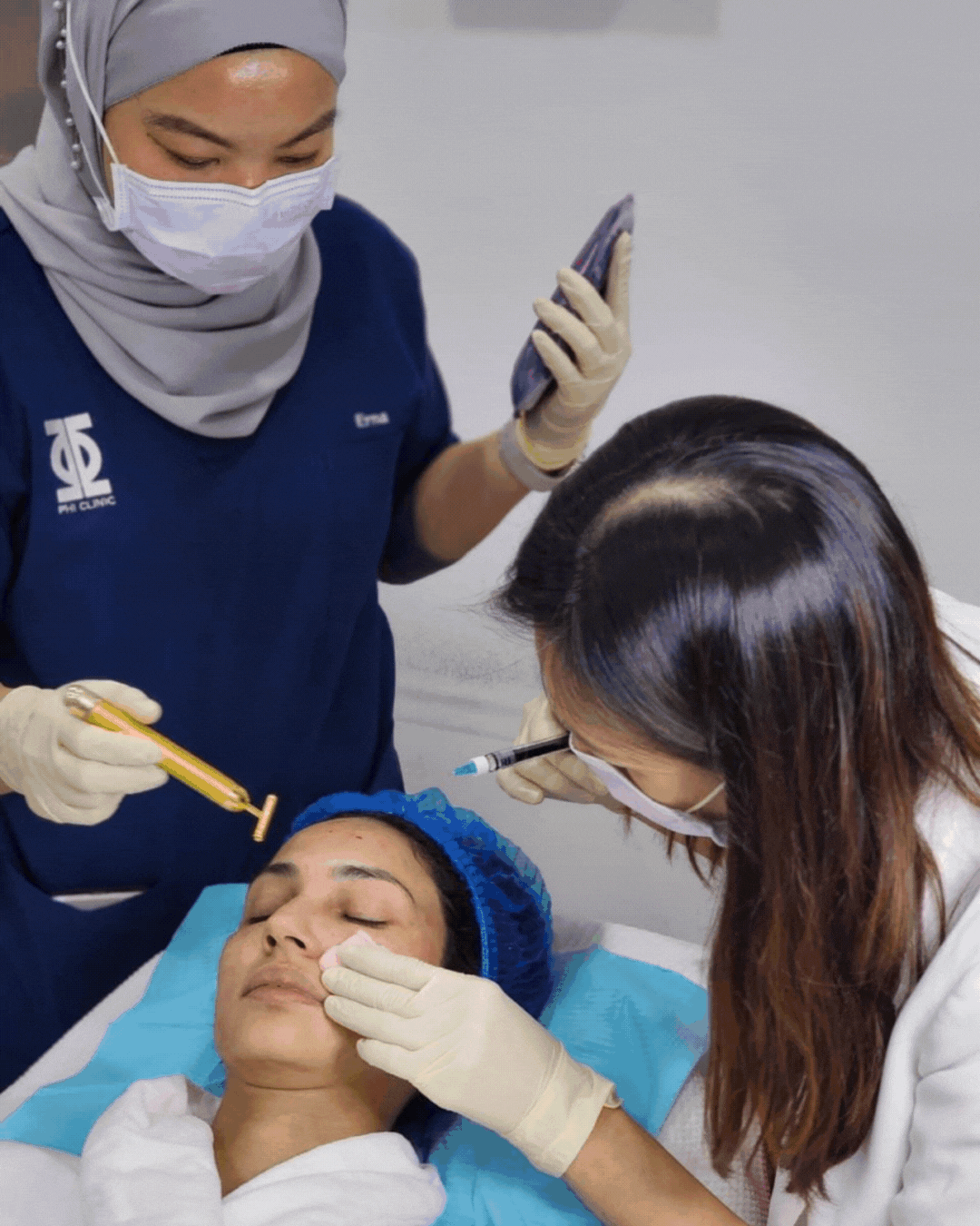 A woman receiving a cosmetic injection procedure on her face in a clinic, with two medical professionals assisting, one holding a syringe and the other holding a pen to examine or mark her skin.