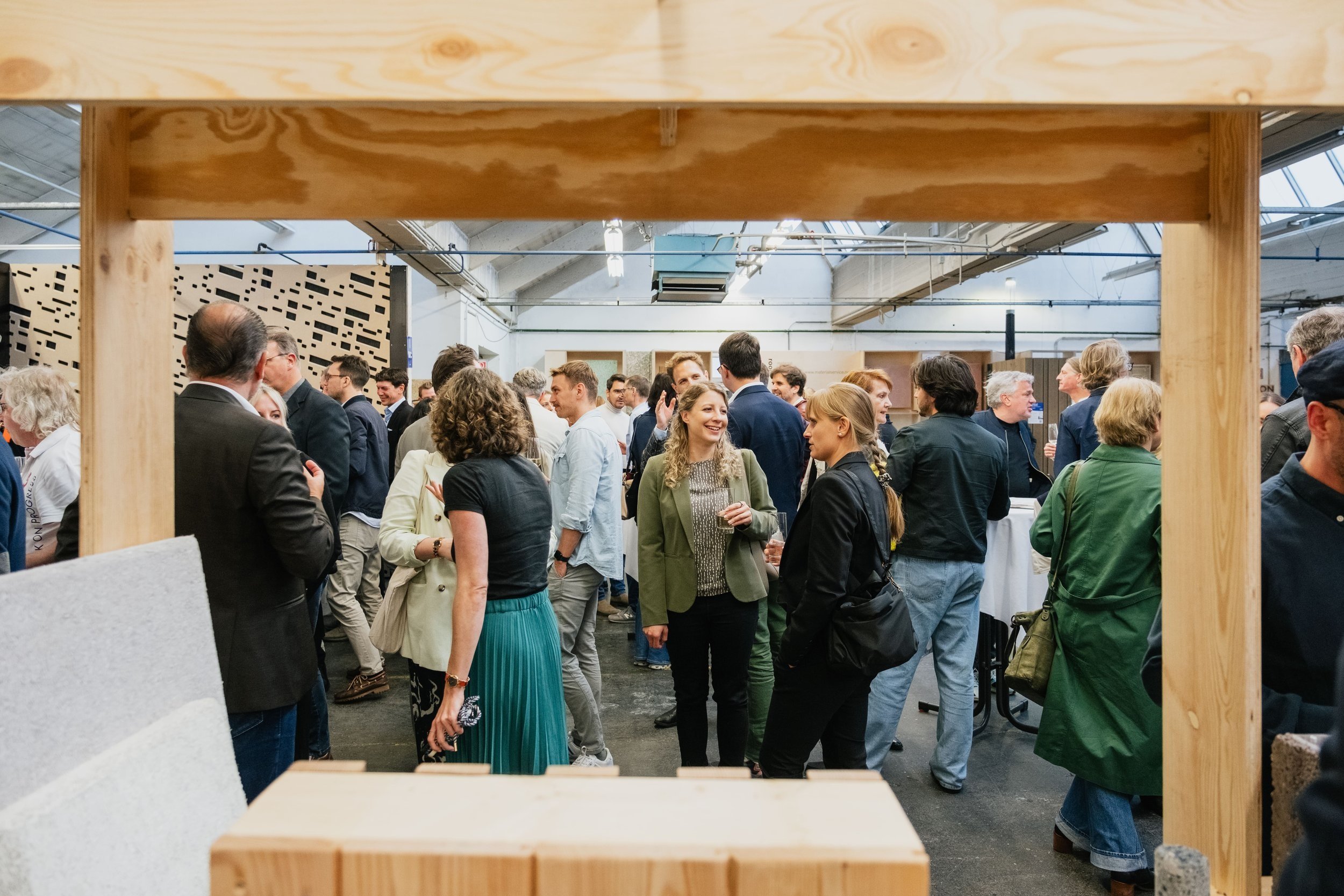 Menschenmenge amüsiert sich, Blick durch Holzregal, nachhaltige Baustoffe im Hintergrund, Industriehalle als Eventlocation