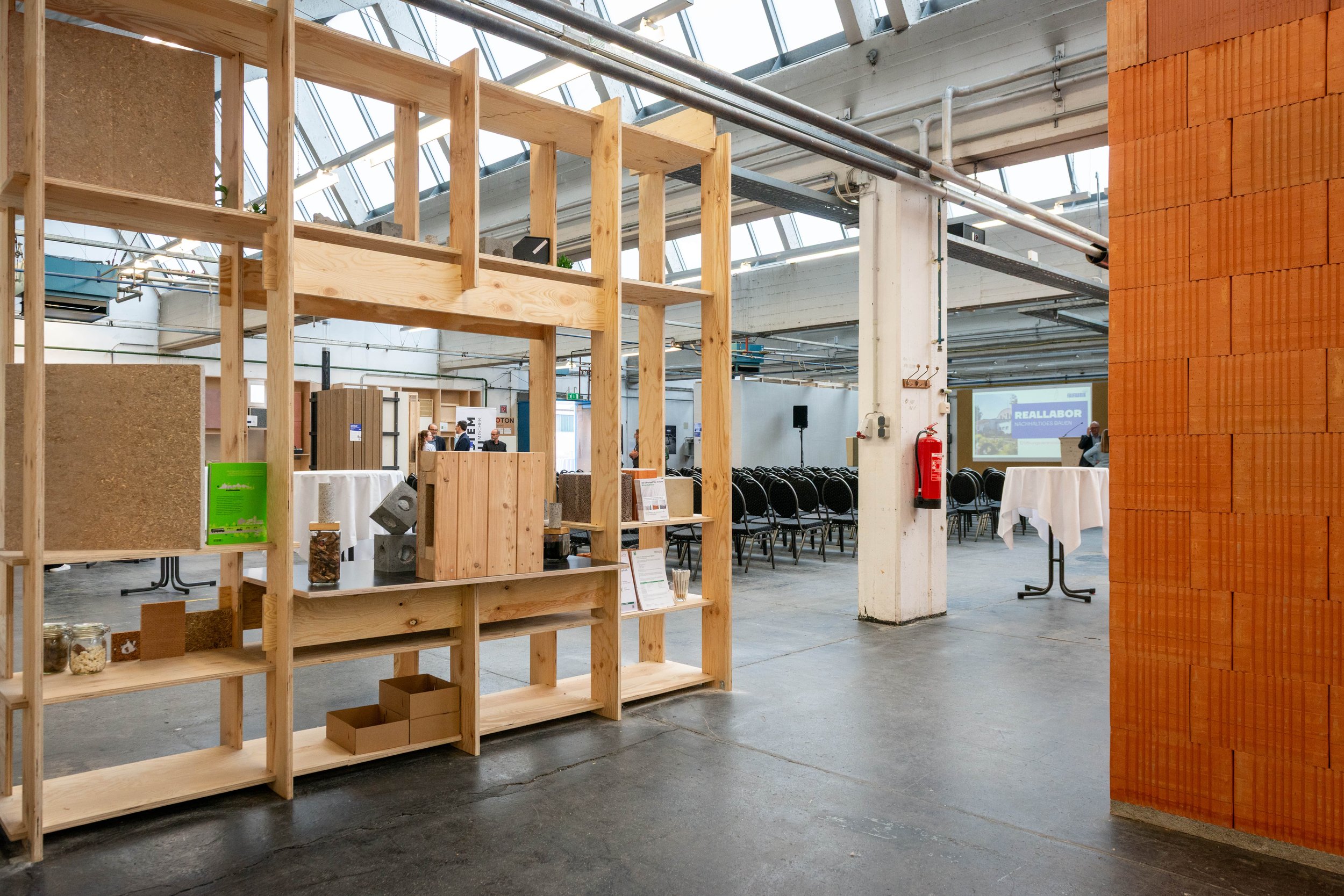 Lagerhalle mit Regalen, voll mit nachhaltigen Baustoffen, Ziegelwand an der rechten Seite, Halle im Industrie-Look