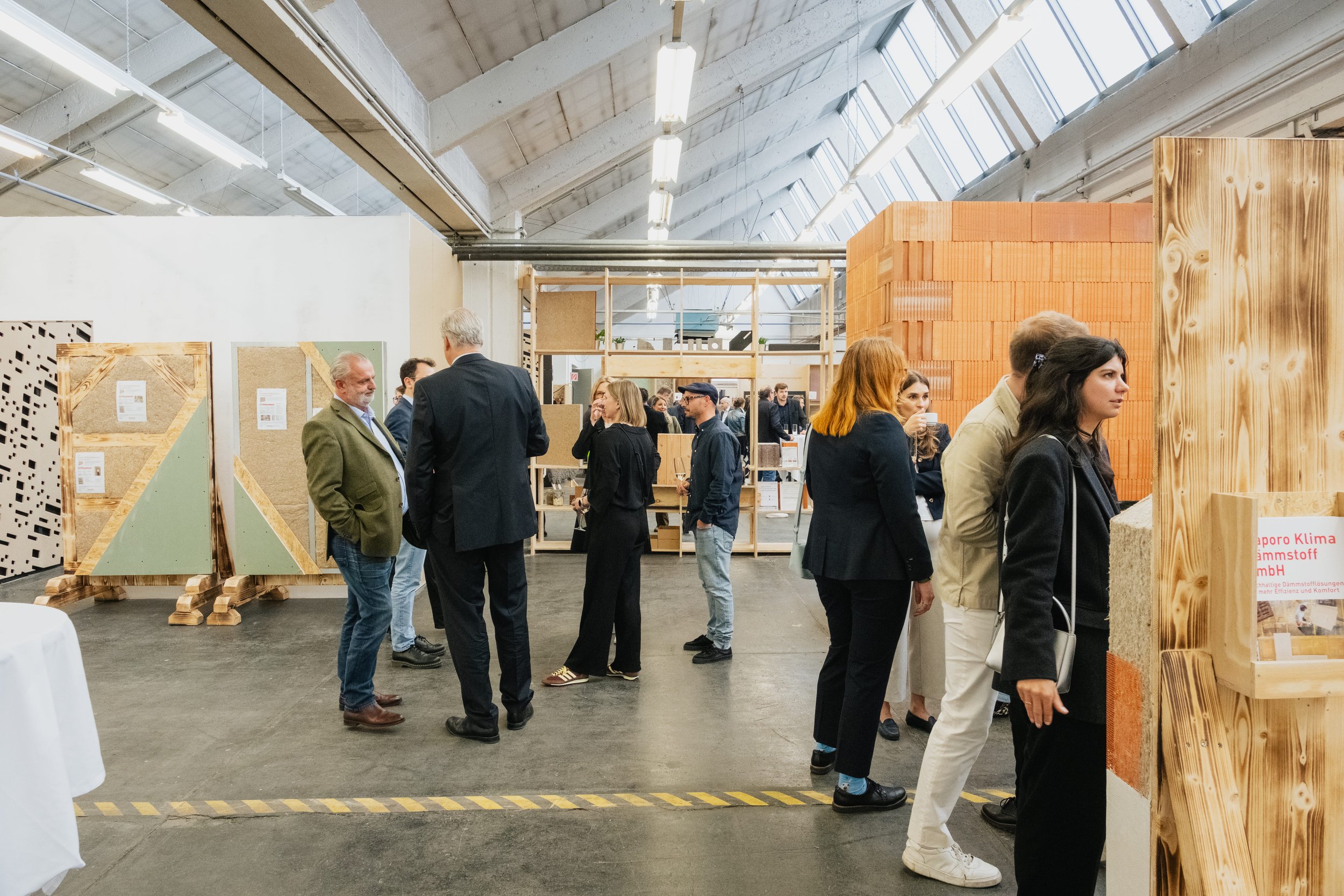 Große Halle im Industrielook, Wand aus Ziegeln und aus Holz, Menschen sprechen.