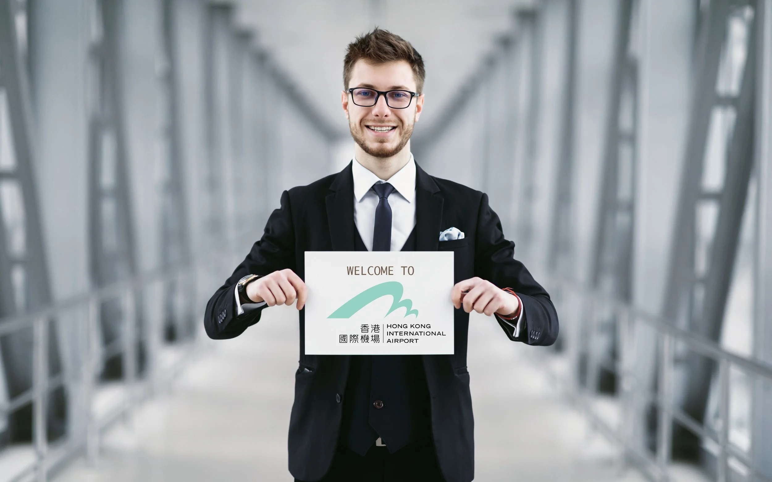 Man in suit holding 'Welcome to Hong Kong International Airport' sign