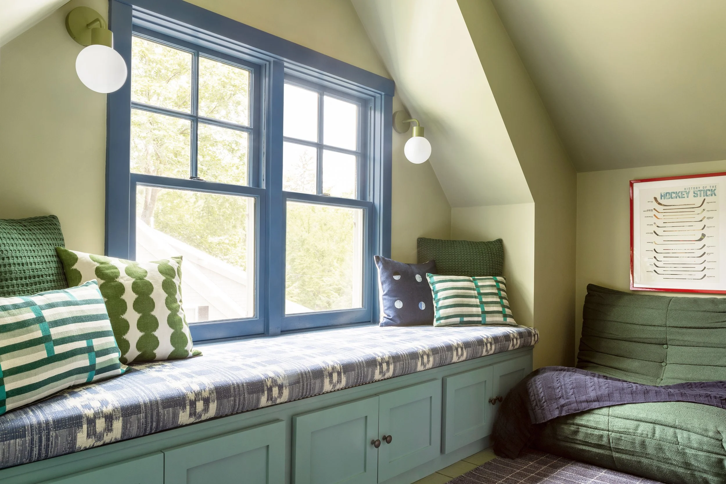 A long window seat sits under an attic eave window. Bright textiles bring pattern and color to the space.
