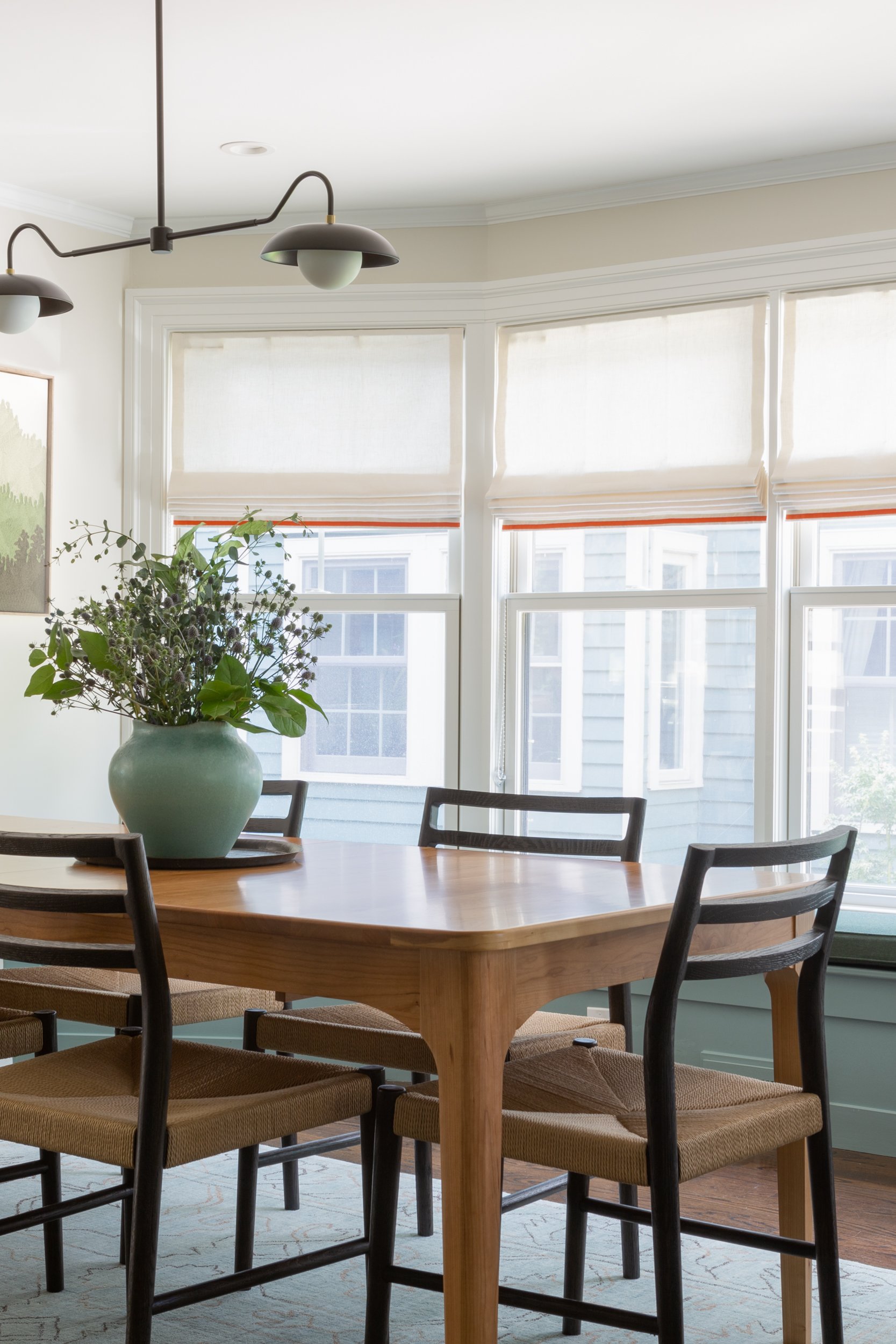 A dining room with a natural cherry parsons table, black rush seat chairs, and a bay window seat.