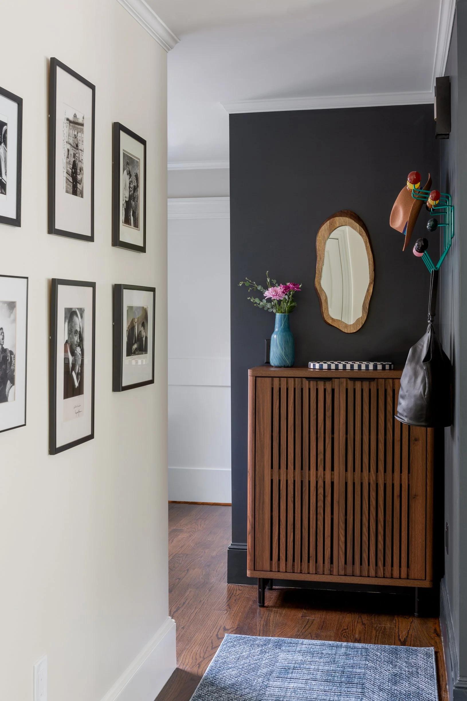 An entryway has cream colored walls on one side with a collection of black and white photographs. The back wall is painted Farrow & Ball Railings.