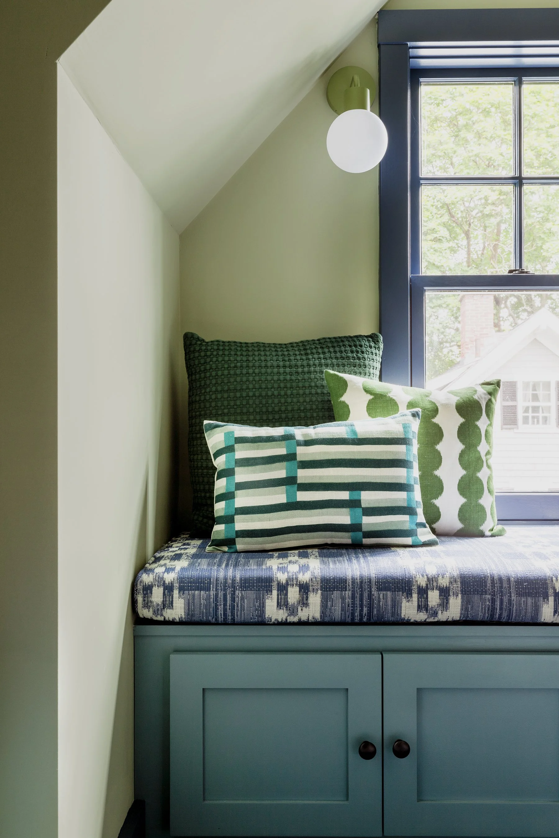 A vignette of an attic room window seat with brightly patterned pillows and cushion fabric.