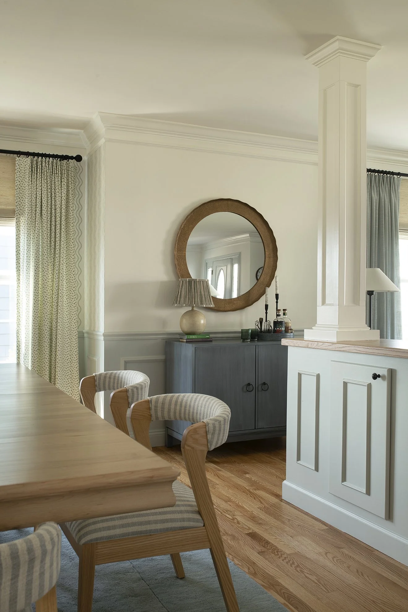 A dry bar divides an open concept living and dining room. A round mirror above the bar expands the space.