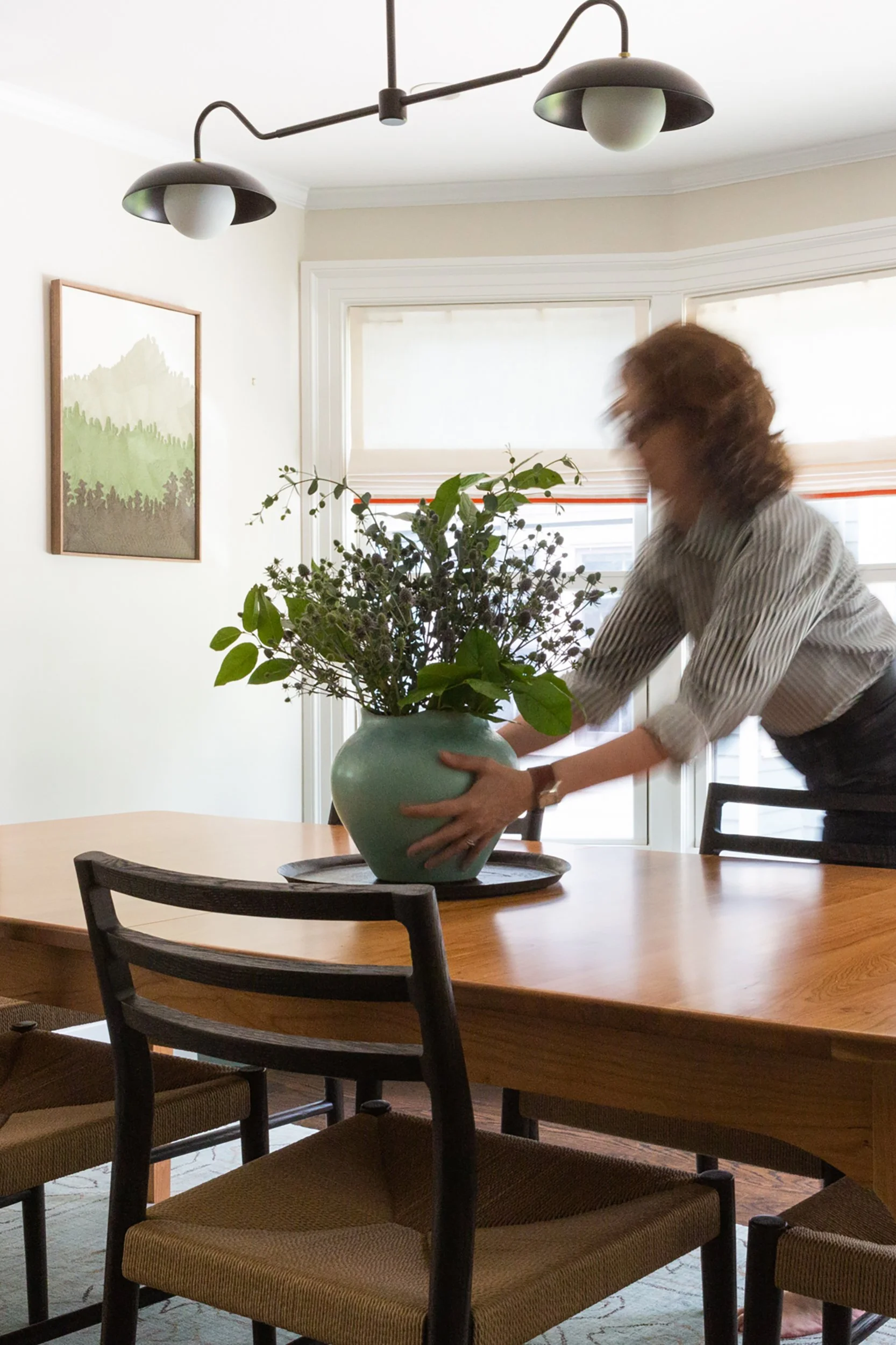 A designer places a vase with flowers onto a dining room table.