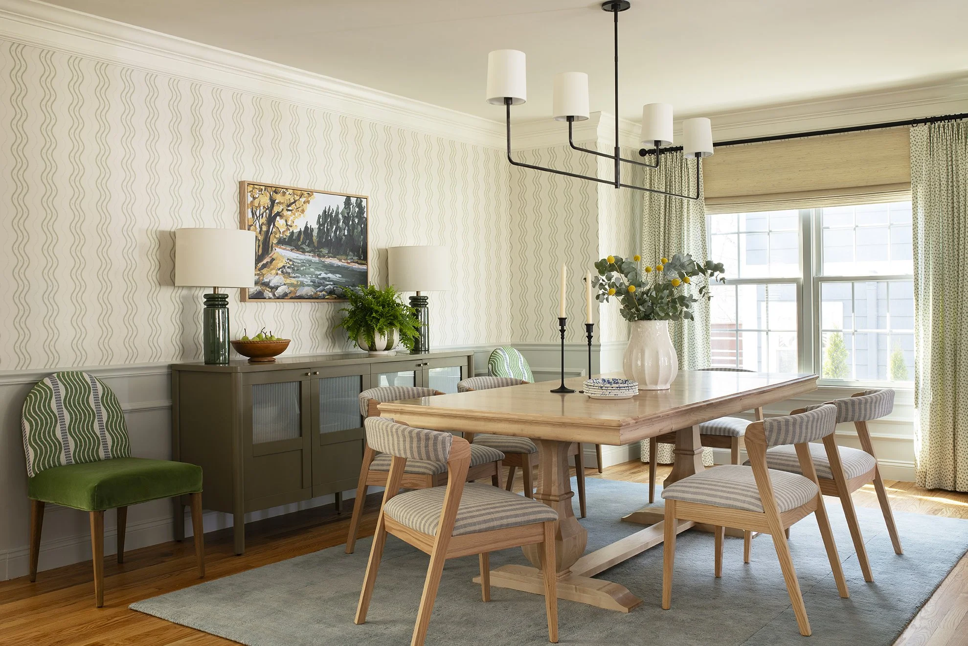 A transitional dining room with Swedish striped wallpaper, a custom maple dining table, layered window treatments, and oak upholstered dining chairs.