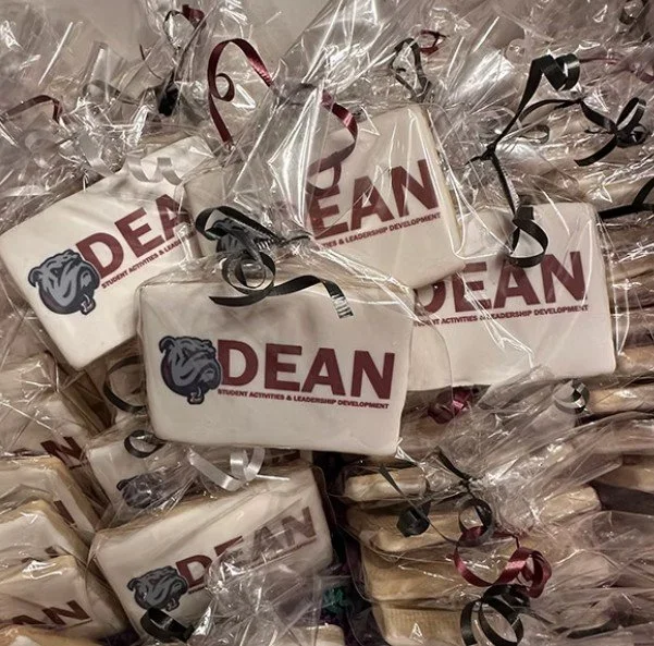 Cookies decorated with 'DEAN' and a bulldog logo, individually wrapped in clear plastic bags with black and maroon ribbons.