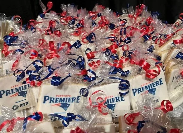 Bags of Patriots Premier merchandise wrapped in clear plastic with red, white, and blue curly ribbons on top, arranged in a pile.