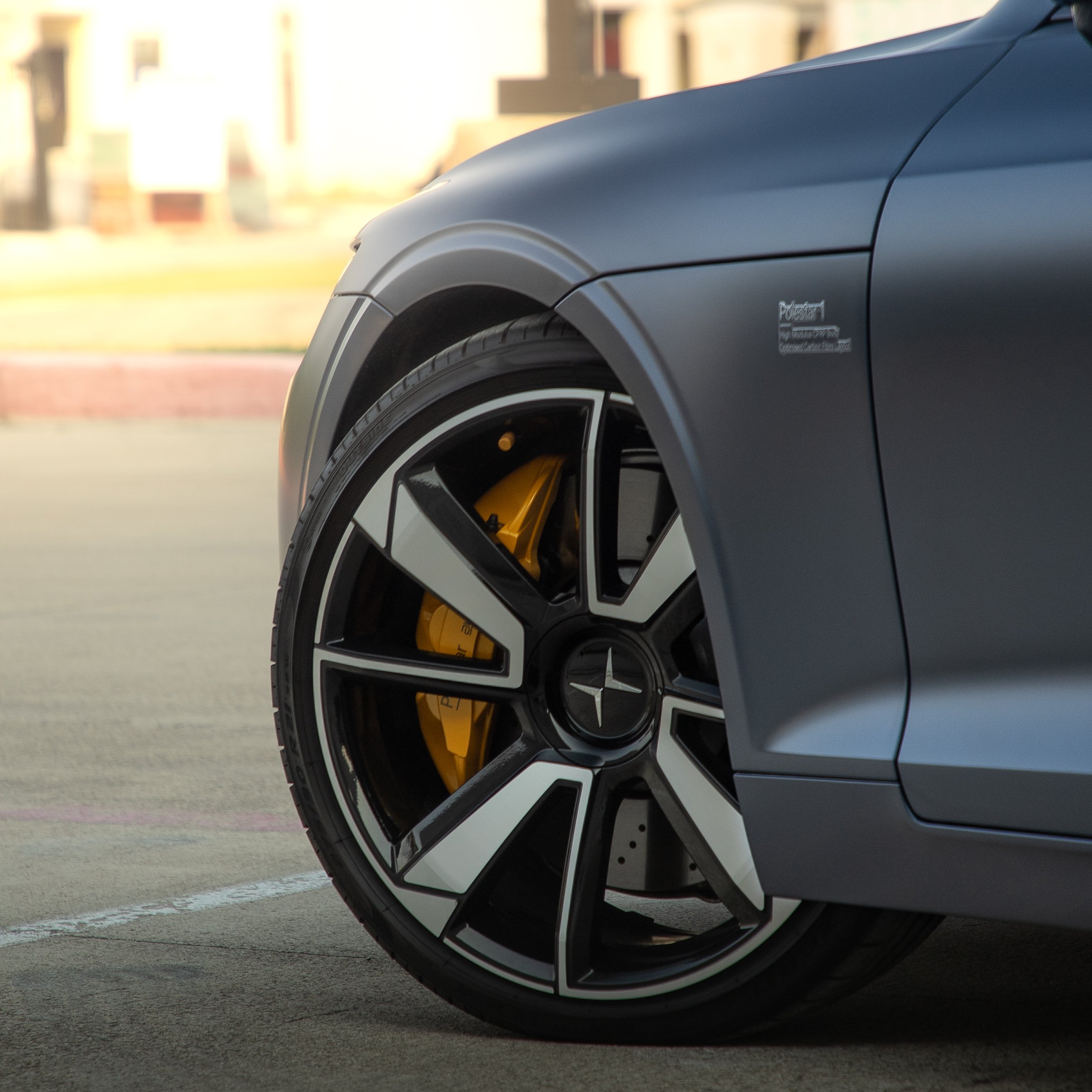 Close-up of car wheel and fender, Polestar logo, yellow brake caliper visible.