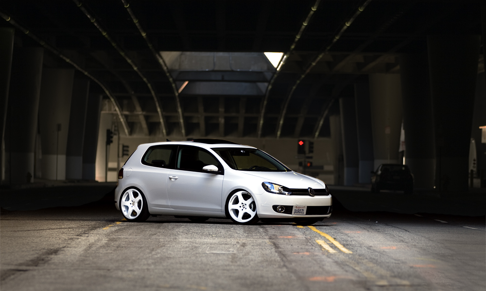 White Volkswagen Golf parked under an urban bridge at dusk