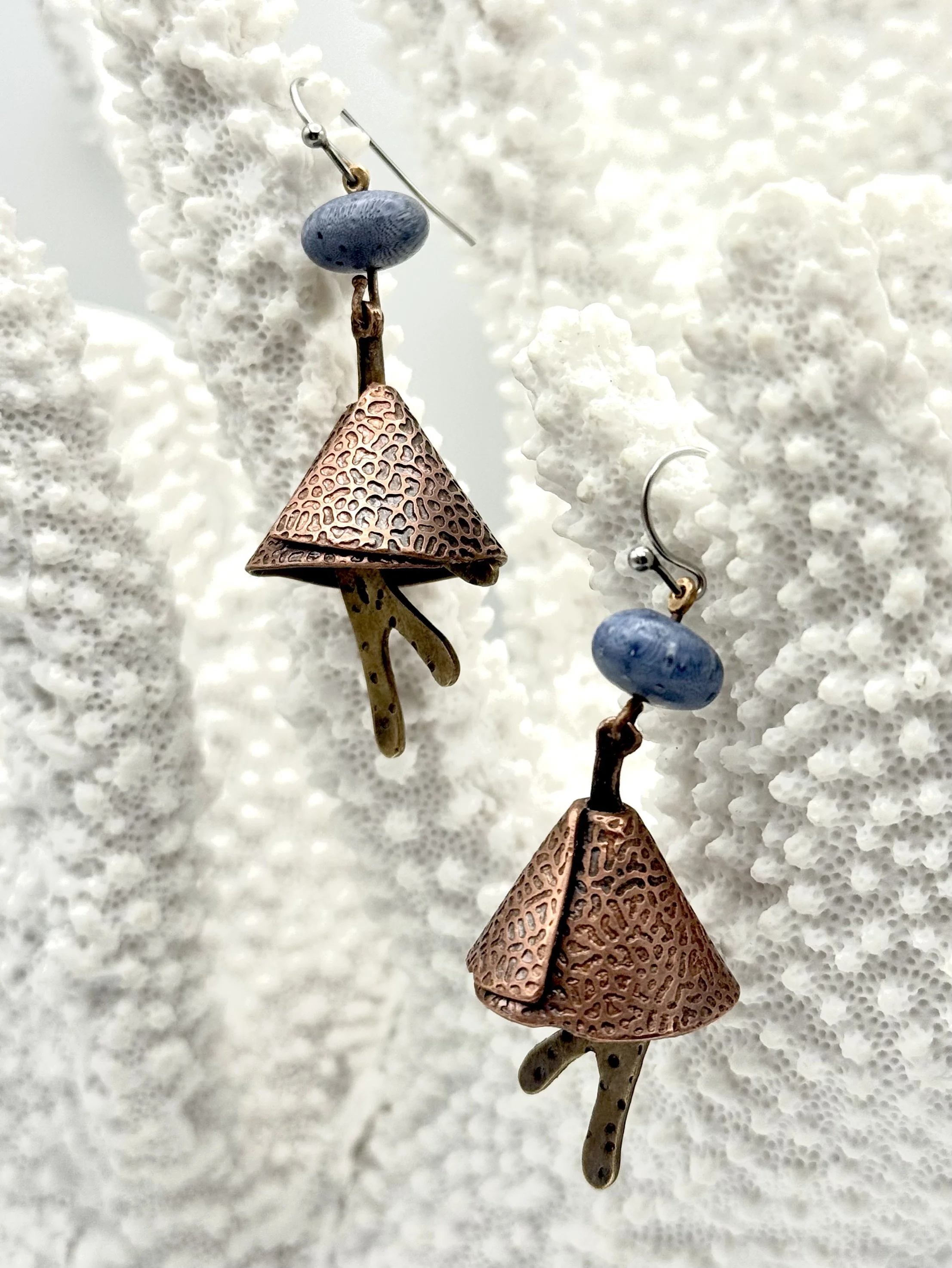 Pair of earrings with copper, bronze, blue fossilised coral beads, and abstract metal pendants, hanging against a white coral background.