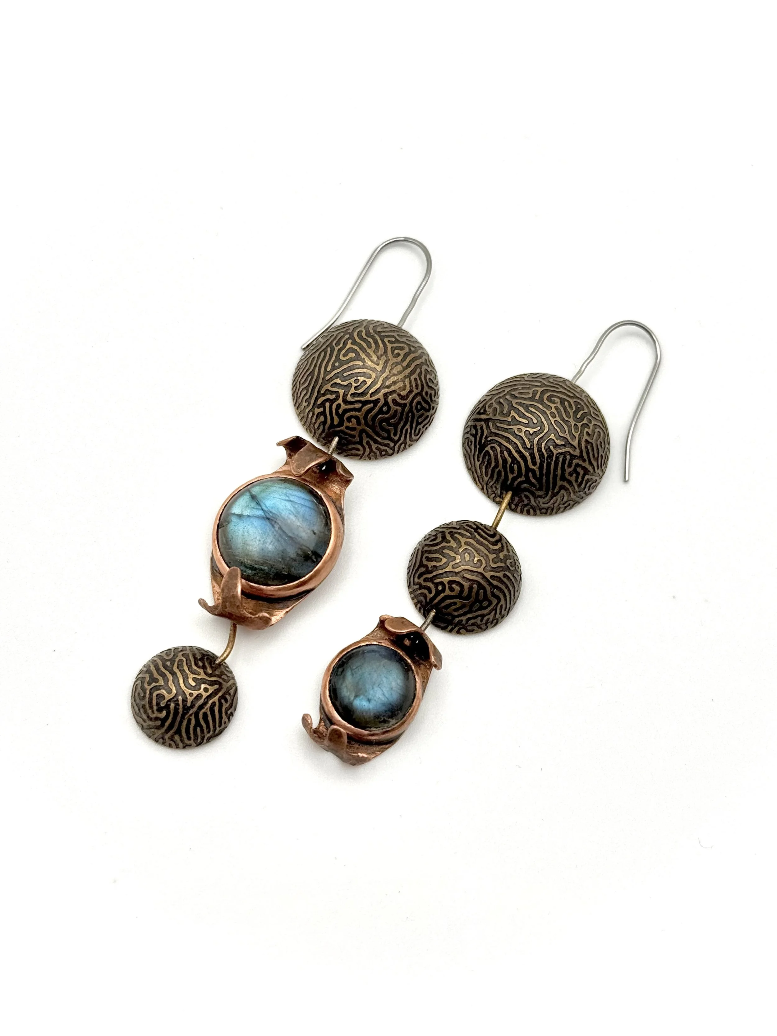 Closeup of a pair of earrings with brain coral textured brass domes and copper cupped labradorite bezels linked together with brass staples and stainless steel ear wires.