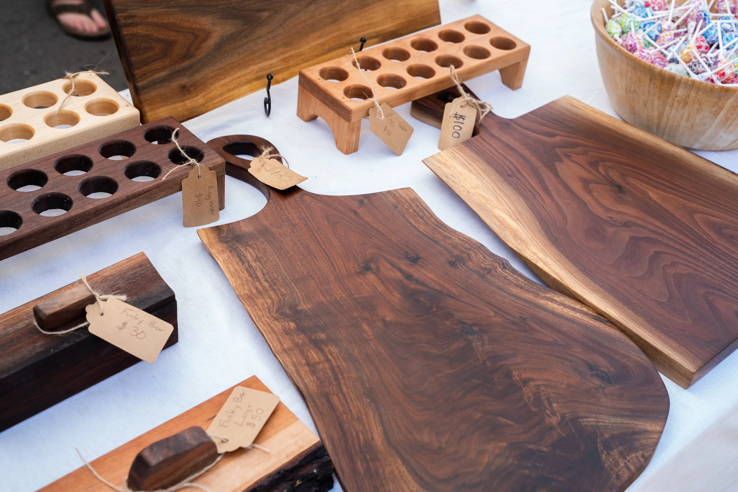 Various wooden serving boards and trays displayed on a table, with some tagged with prices, alongside a bowl of lollipops.