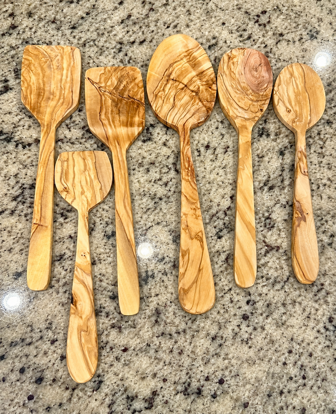 Set of six wooden kitchen utensils, including spoons and spatulas, with a marbled wood grain pattern, arranged on a granite countertop.