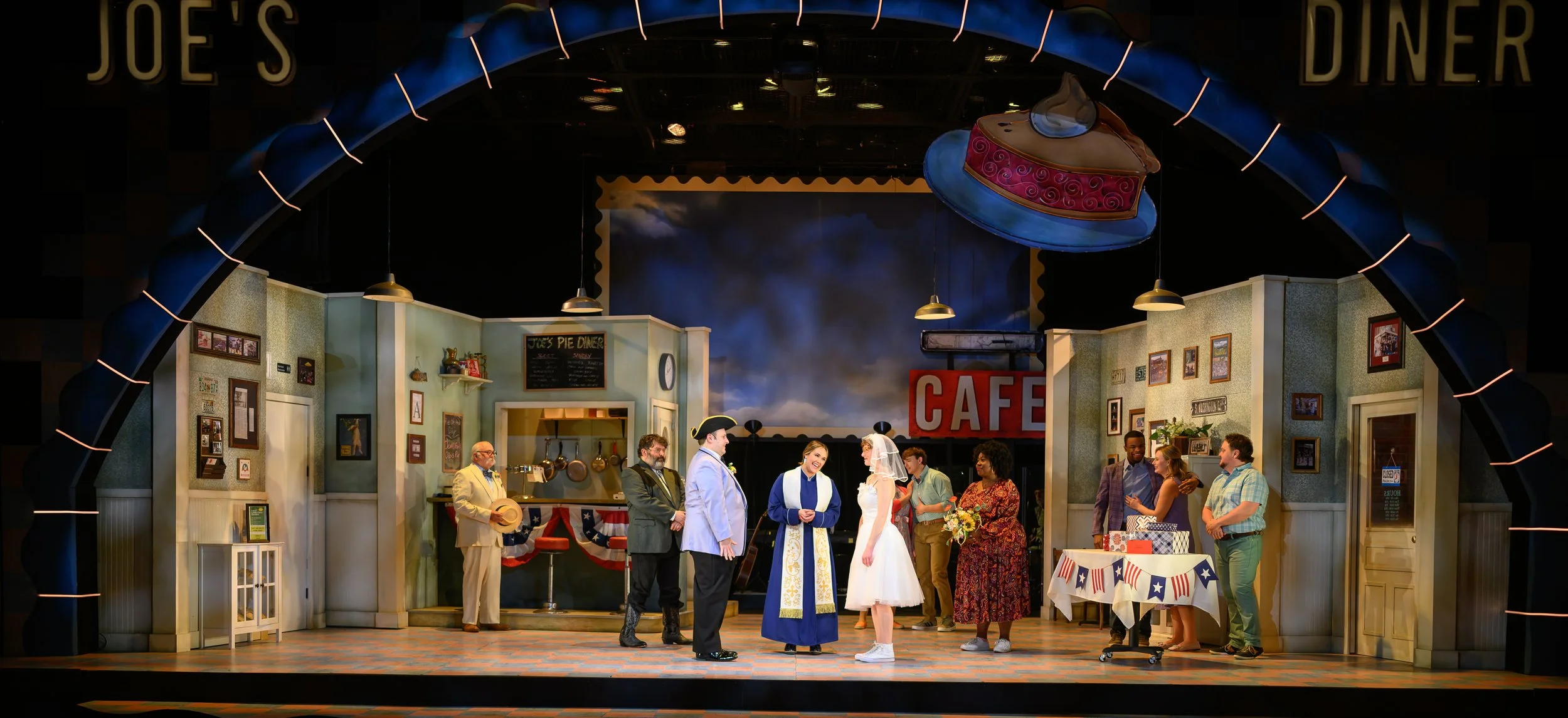 The stage set depicts a scene inside a small American restaurant or diner, with several people gathered, including a bride and groom, possibly part of a wedding scene or celebration.