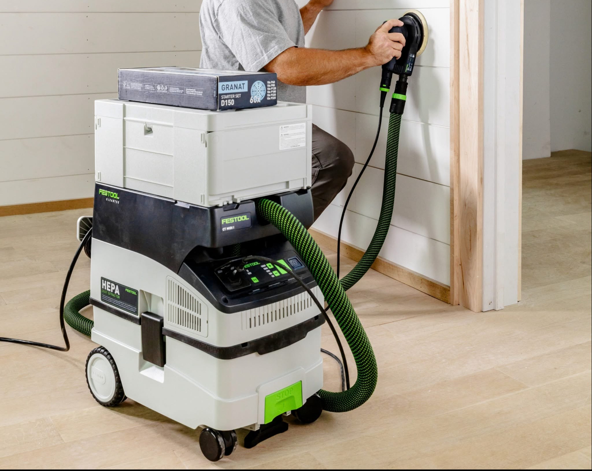 A person using a Festool sander connected to a dust collection system.